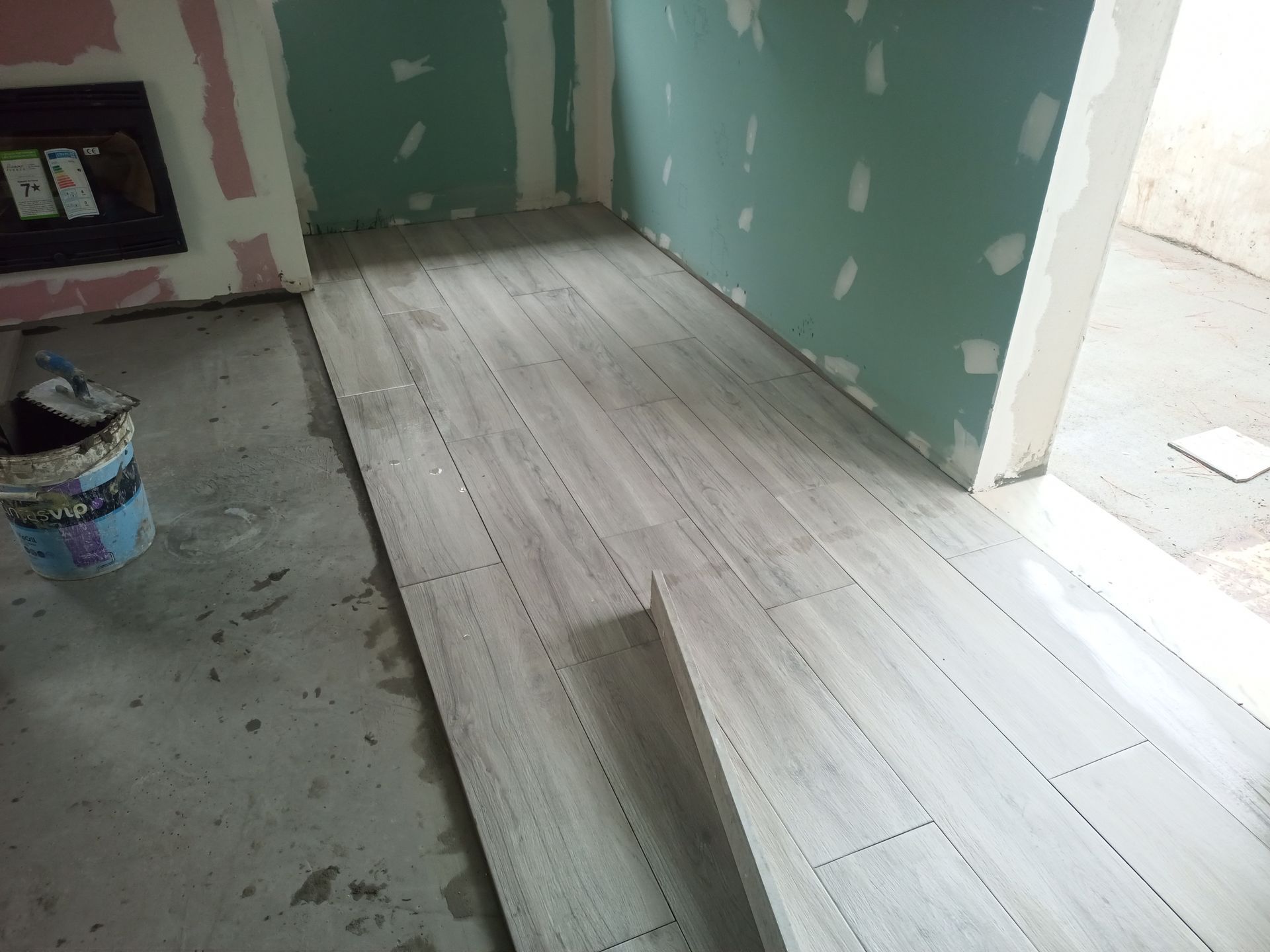 Instalação de piso cerâmico imitando madeira sobre contrapiso de concreto em um cômodo com paredes parcialmente acabadas.