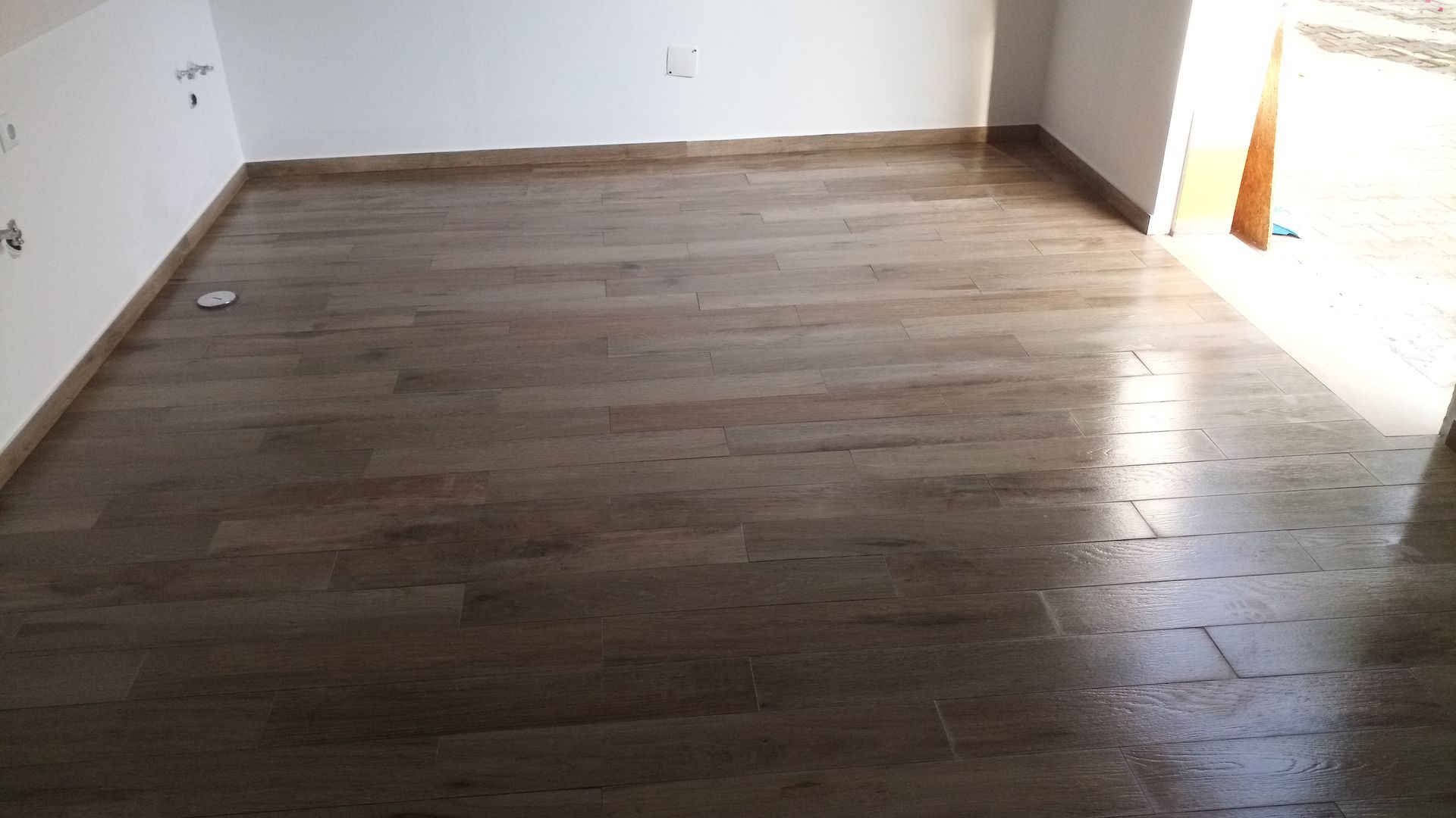 Quarto com piso de porcelanato imitando madeira e paredes brancas. A porta fica à direita.
