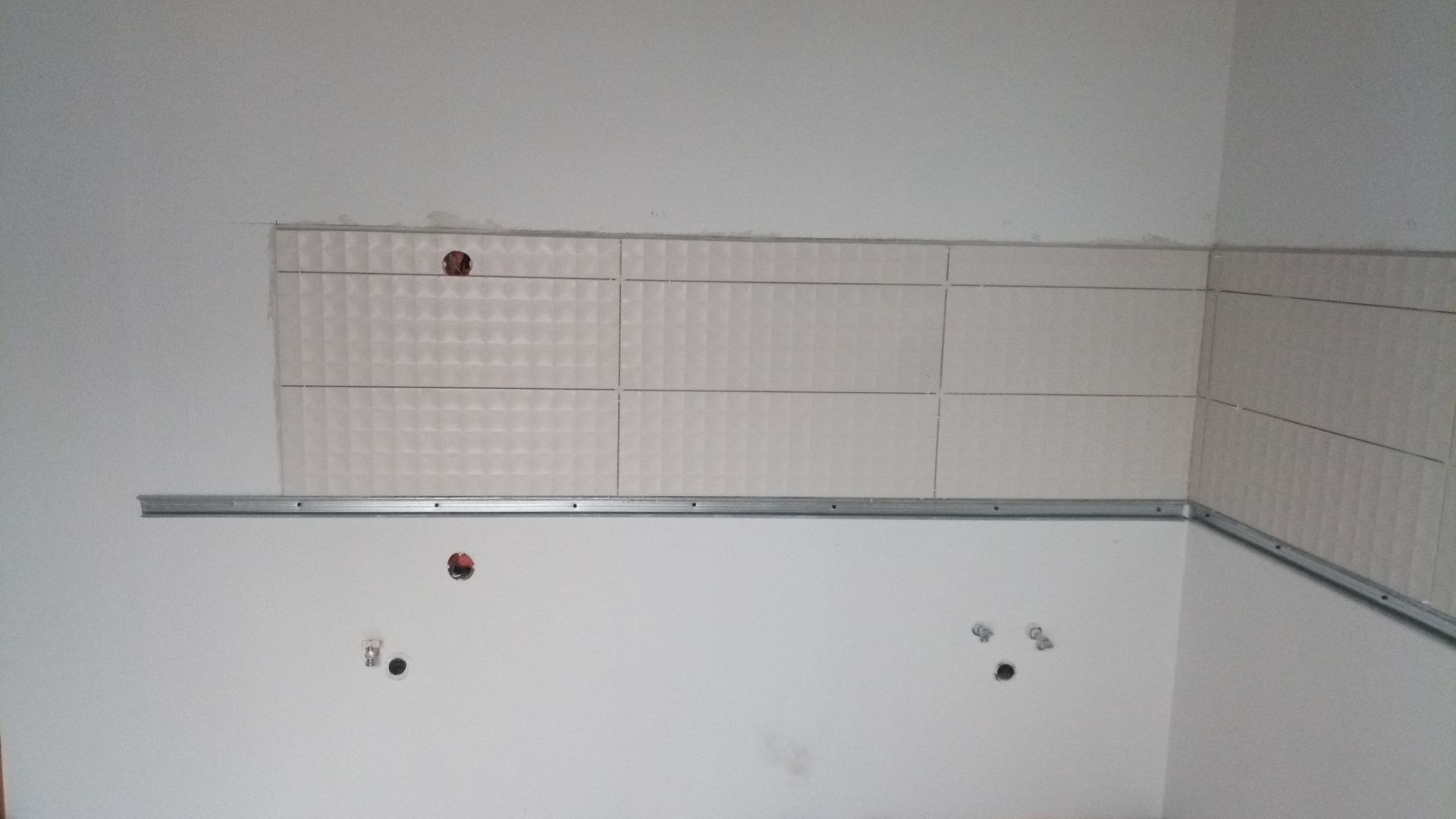 Parede branca com suporte metálico instalado e seções de revestimento de azulejos.
