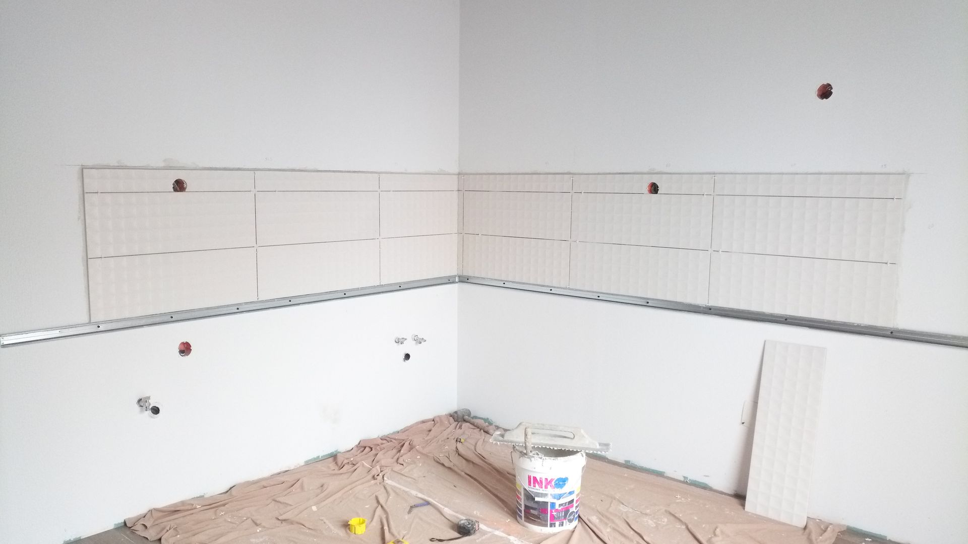 Canto interno com parede de gesso e fiação exposta, preparado para receber azulejos, com um balde de tinta à mostra.