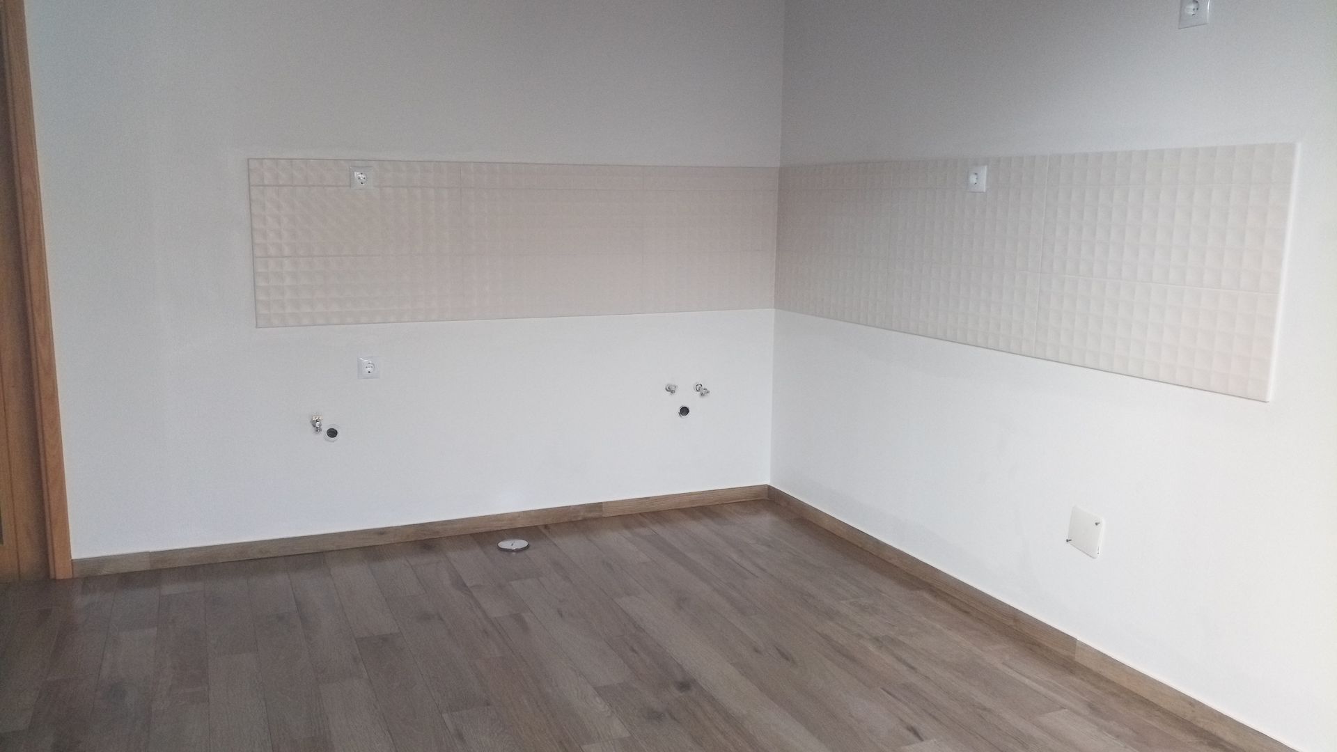 Quarto vazio com piso imitando madeira e paredes brancas. Revestimento bege na parte superior da parede.