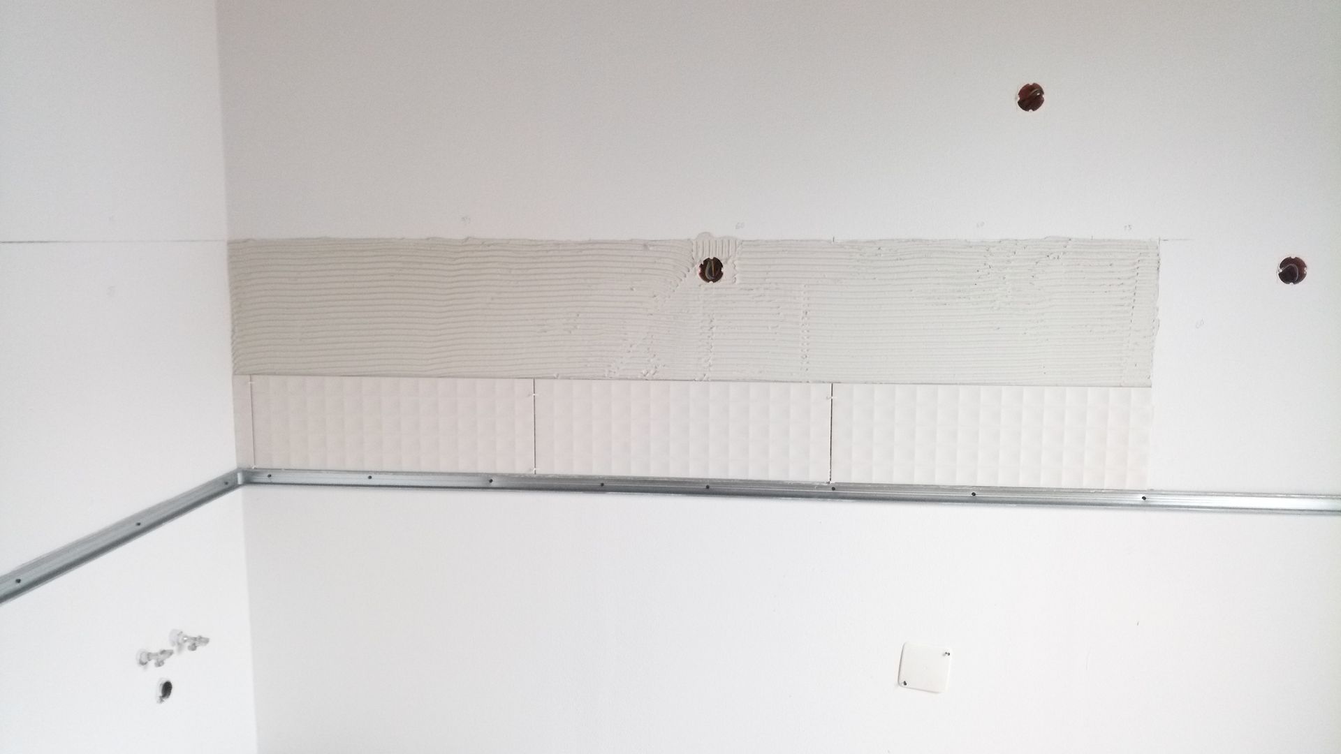 Parede interna com moldura metálica instalada e superfície parcialmente revestida com azulejos.
