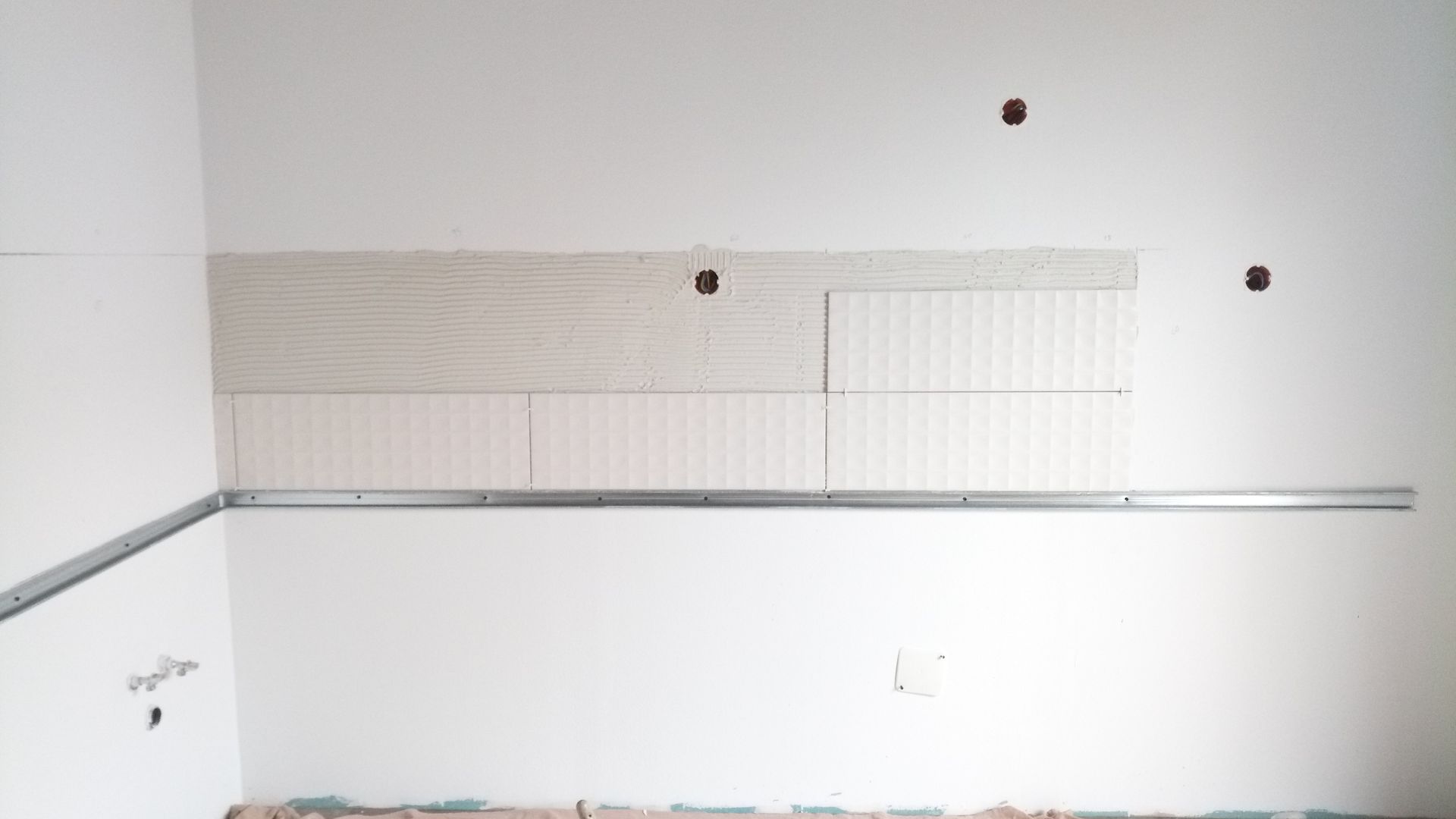 Parede interna com grades metálicas e backsplash parcialmente revestido com azulejos em construção.