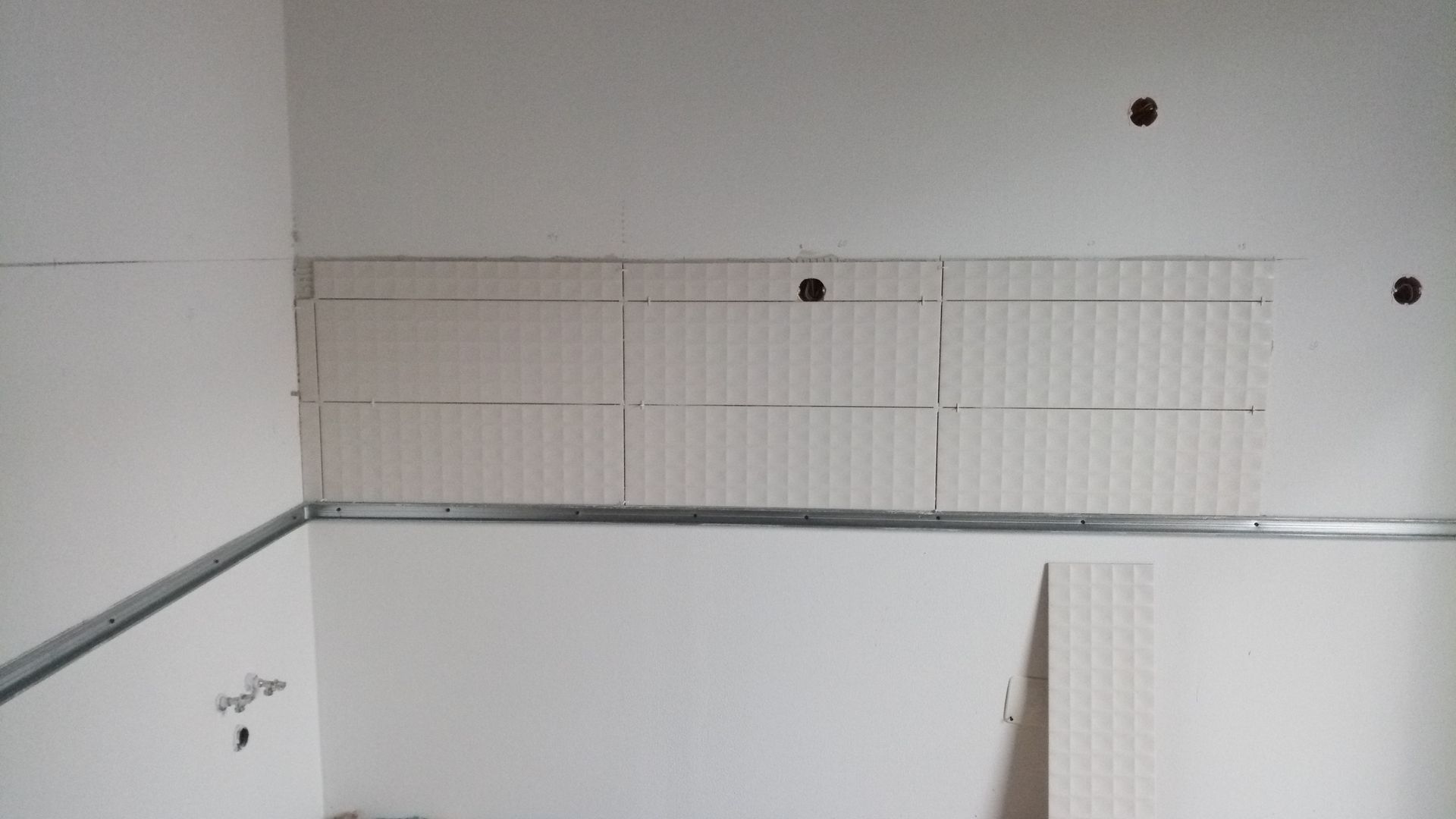 Vista interna de uma sala com instalação de drywall em andamento; trilhos de metal e juntas visíveis.