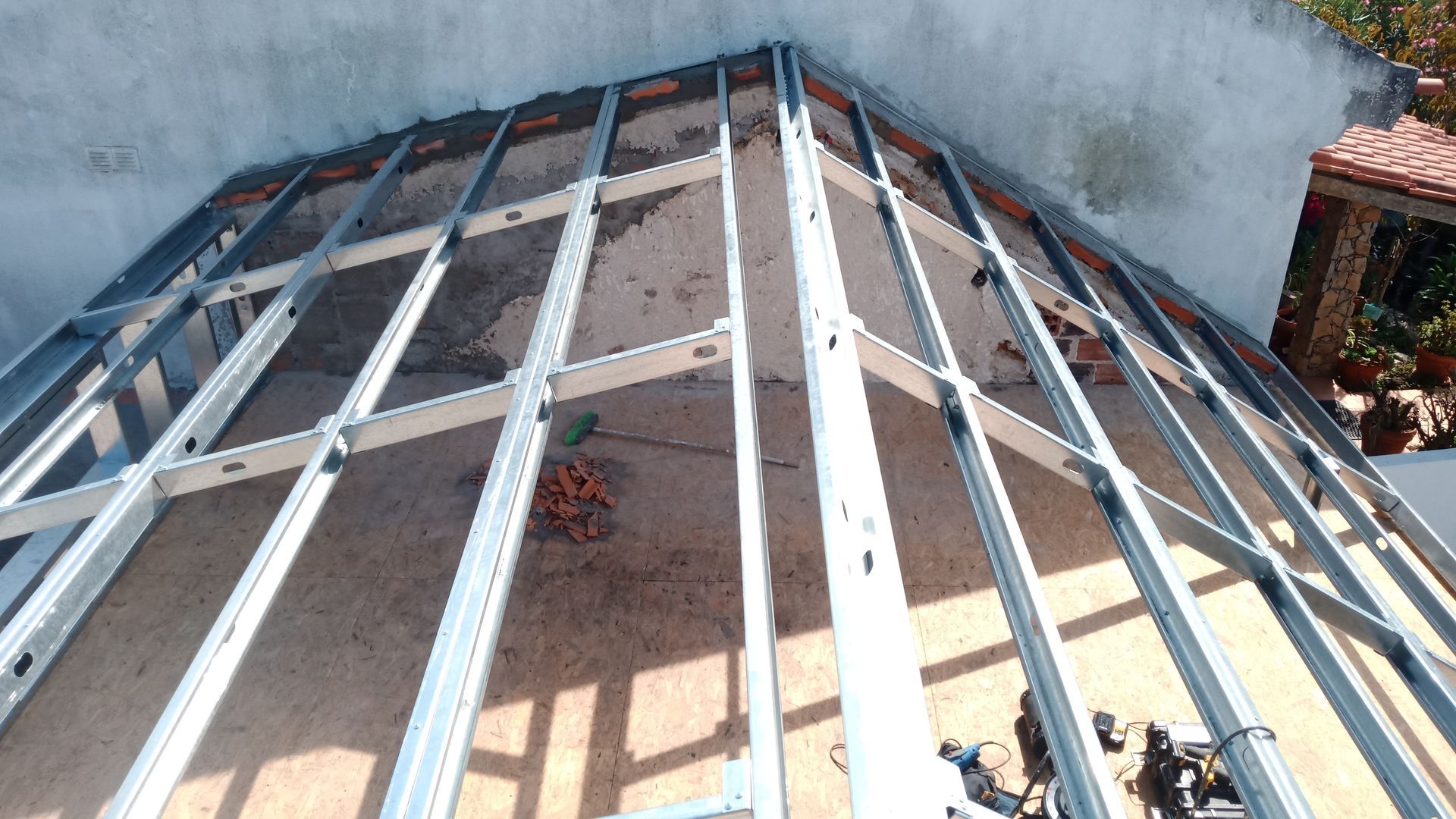 Estrutura metálica para um telhado em construção contra uma parede branca.