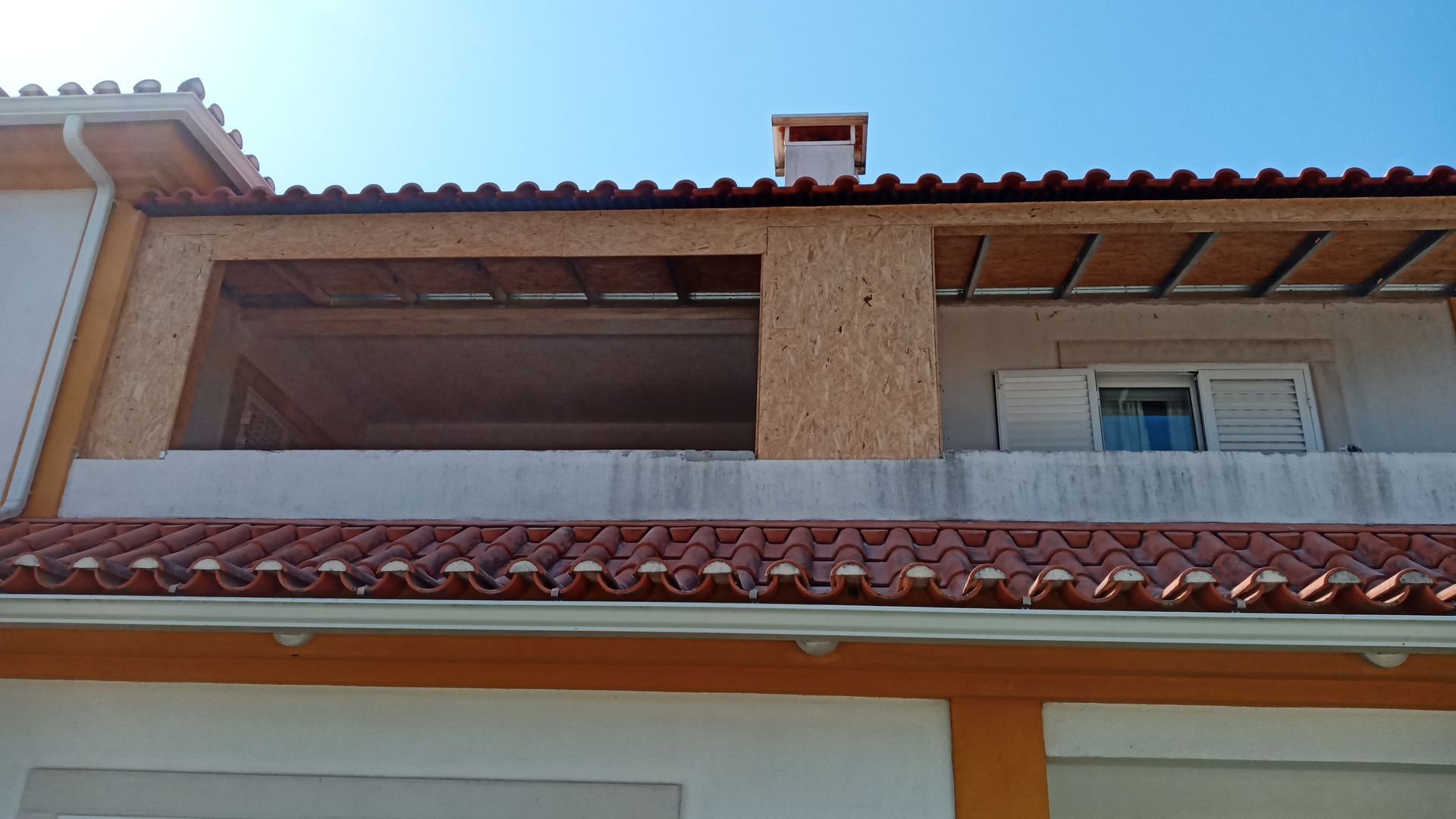 Telhado de telhas laranja de um edifício com uma grande varanda ao ar livre e uma pequena chaminé.