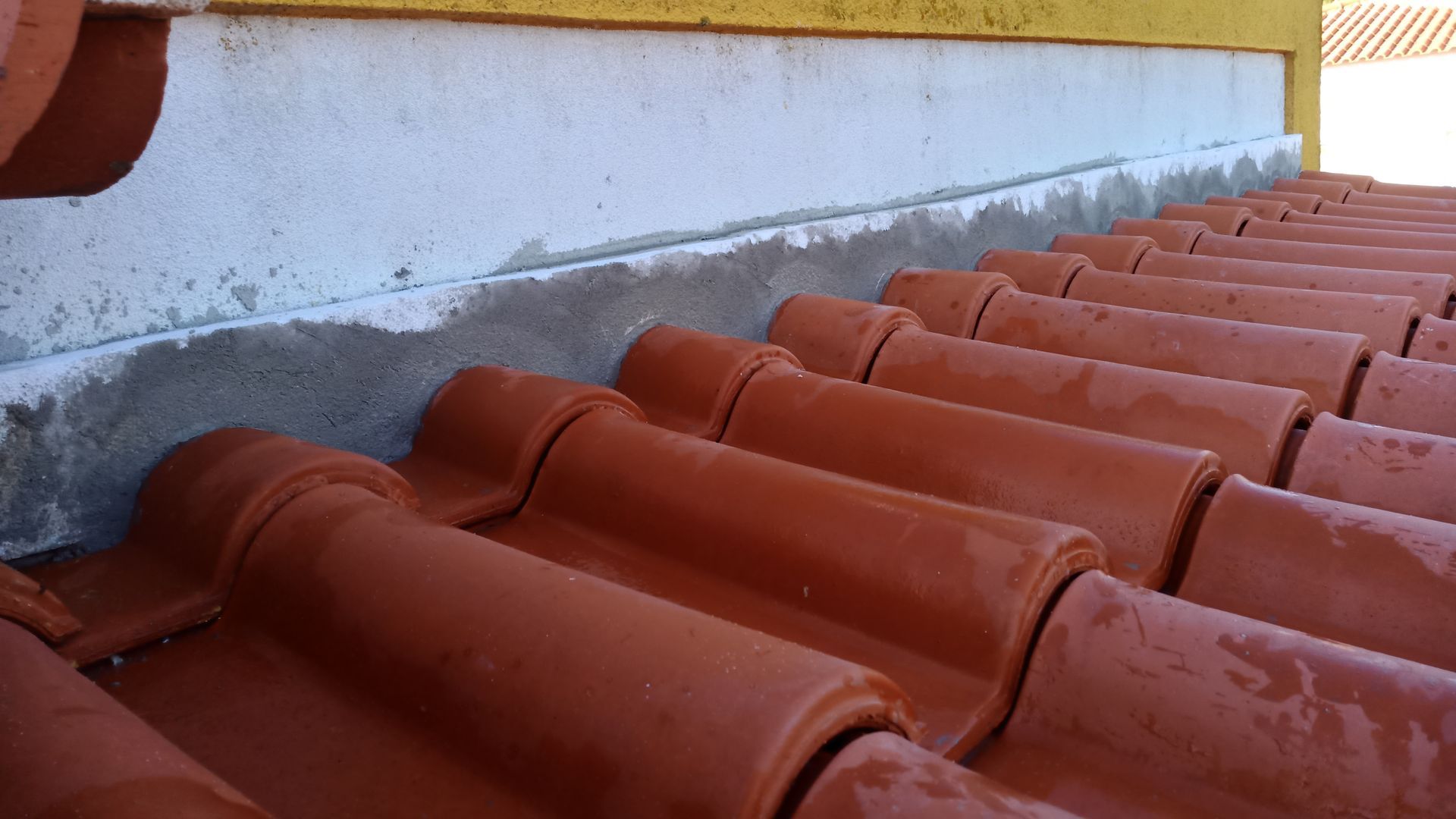 Telhas vermelhas ao lado de uma borda de concreto cinza sob uma parede amarela.
