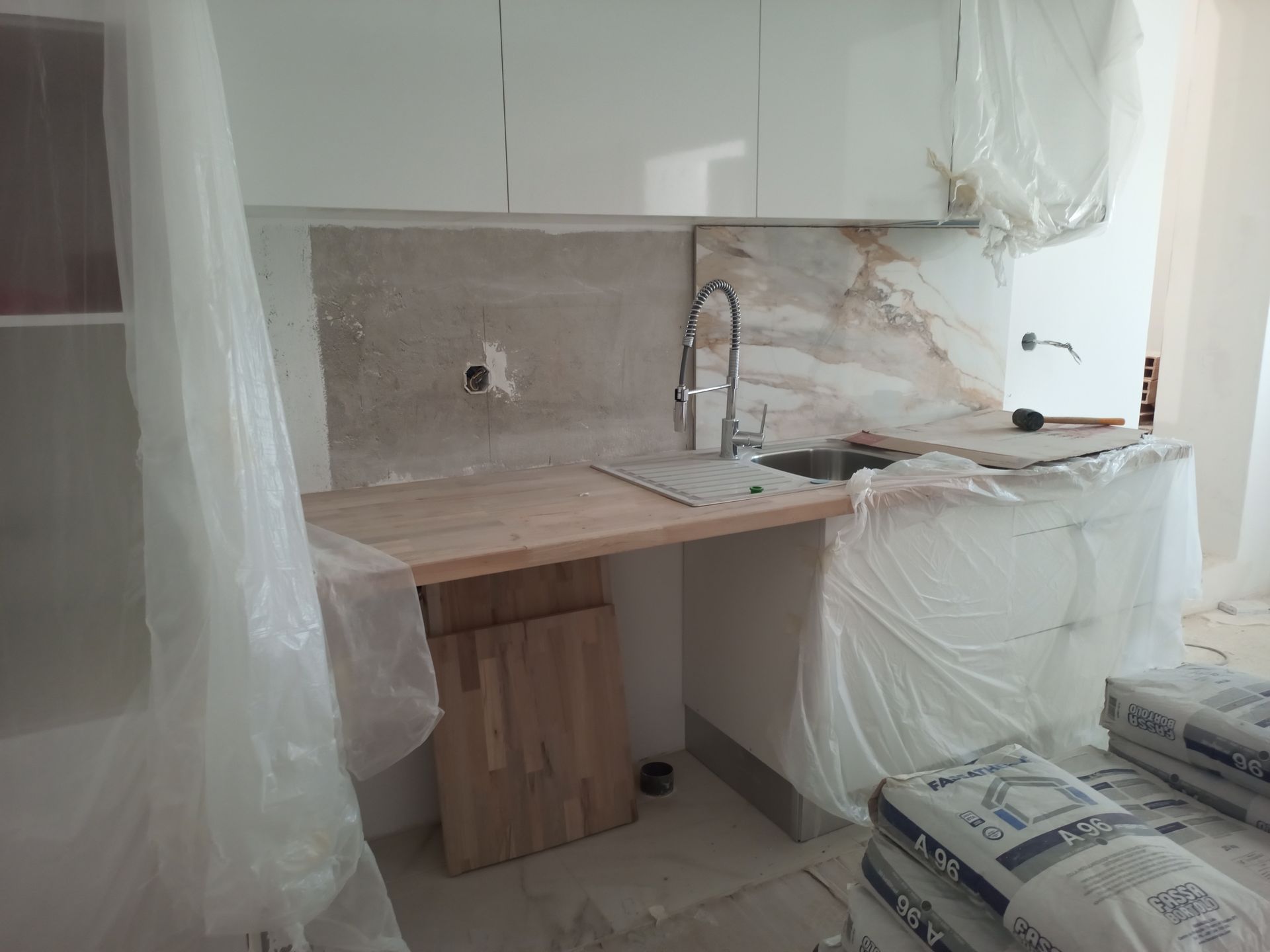 Cozinha em construção com armários inacabados, pia e backsplash cobertos com plástico.