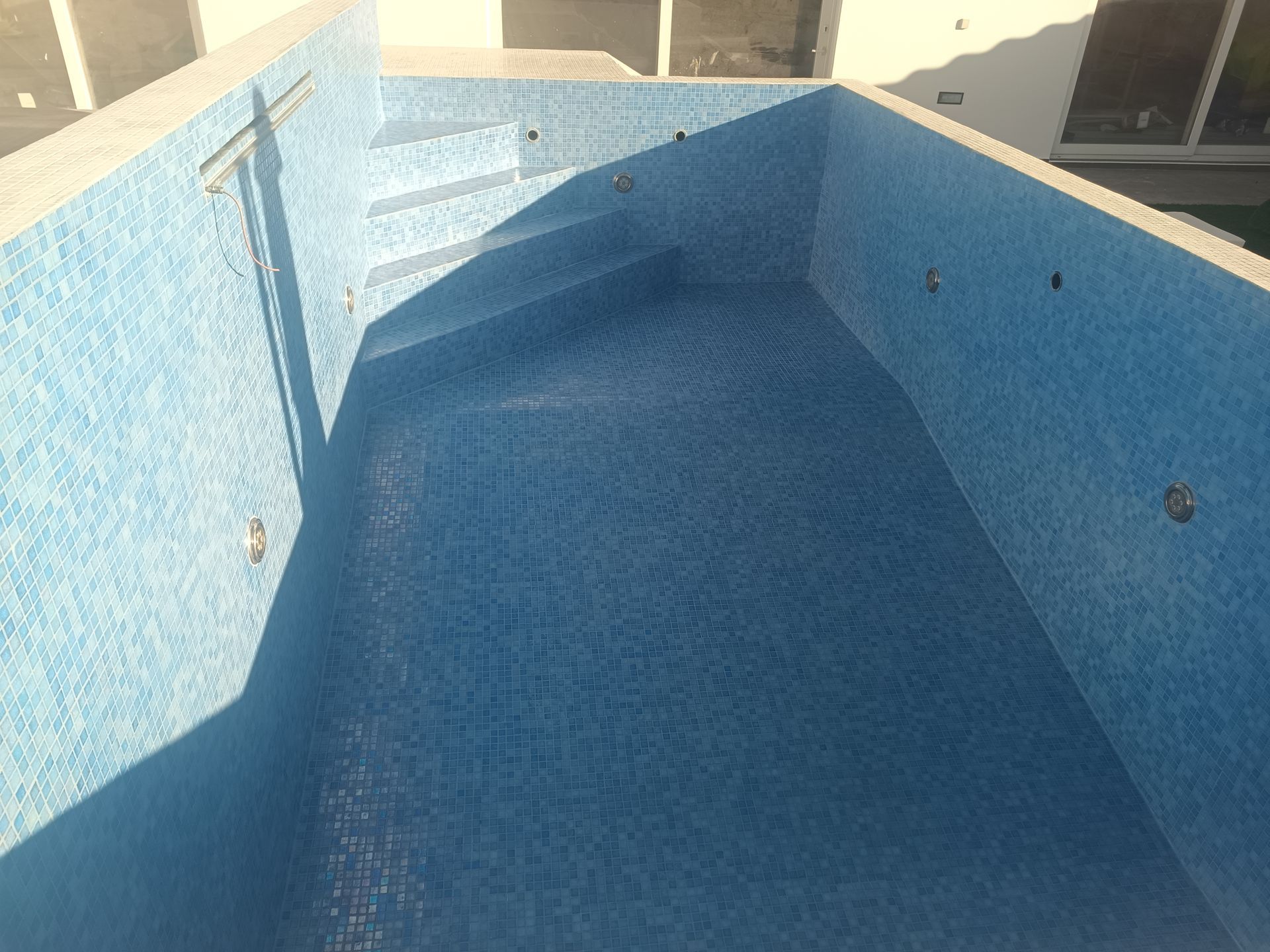 Piscina vazia com interior e degraus revestidos com azulejos azuis, vista de cima.