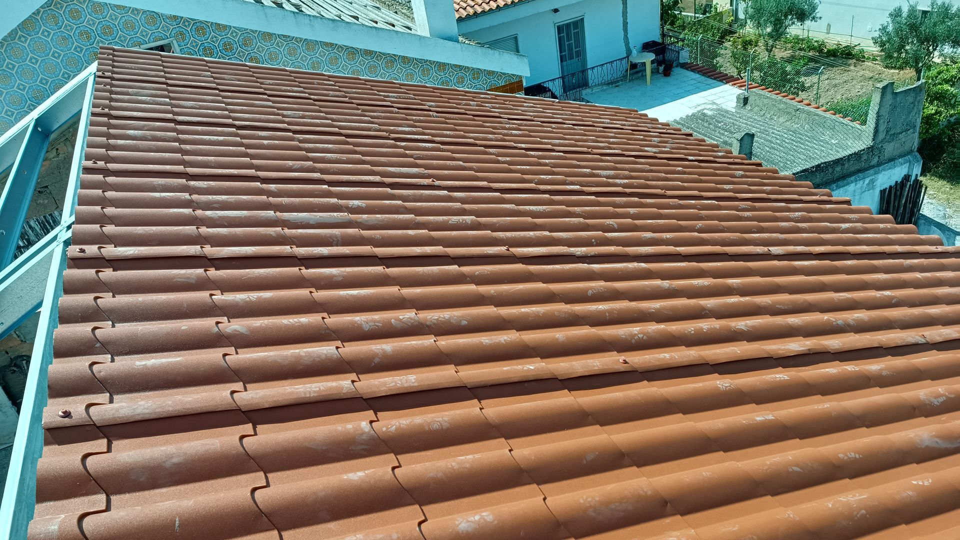 Telhado de telha vermelha, vista de cima, com edifícios ao fundo em um dia ensolarado.