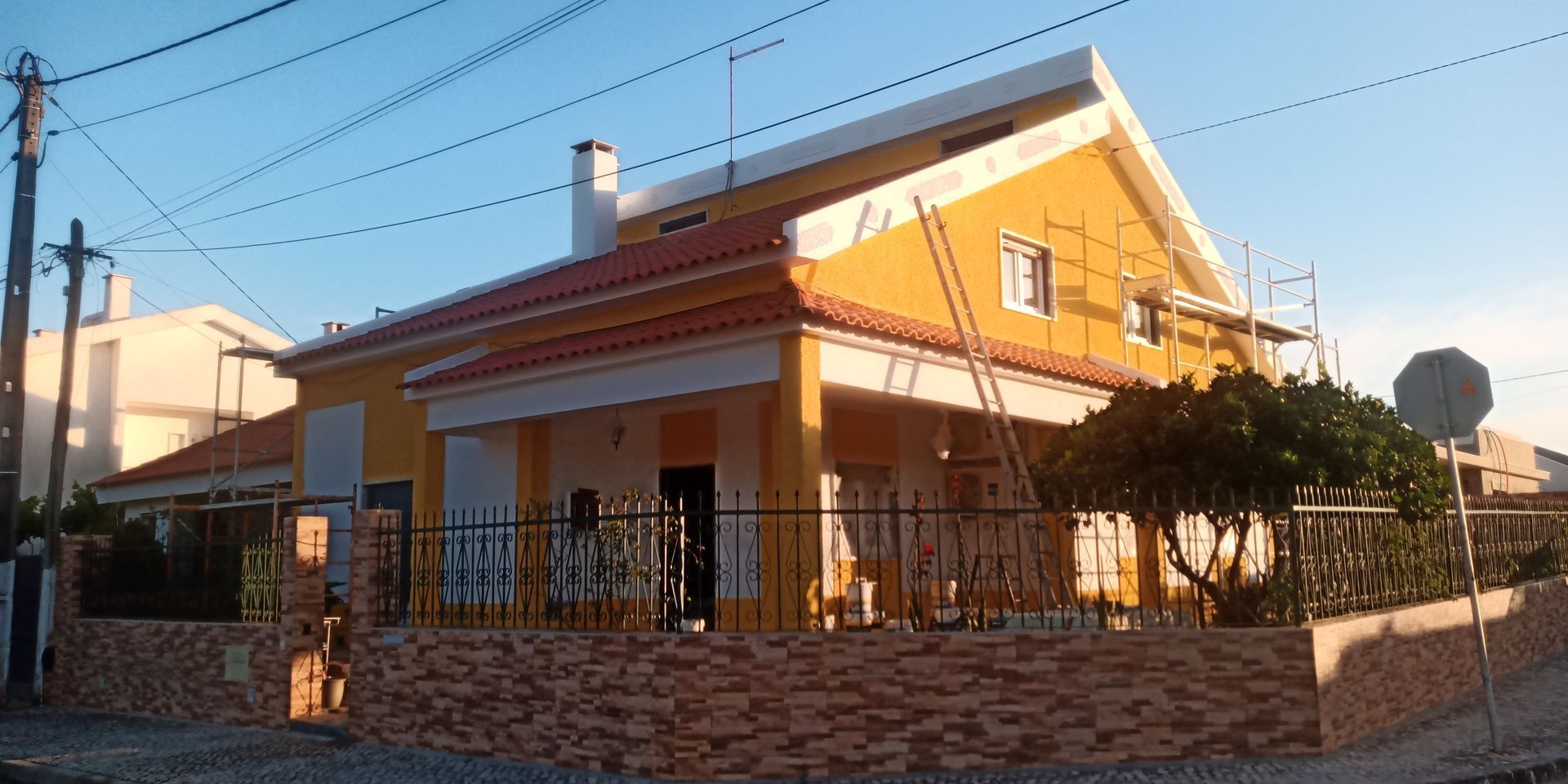Casa amarela com telhado laranja em construção, com andaimes visíveis.