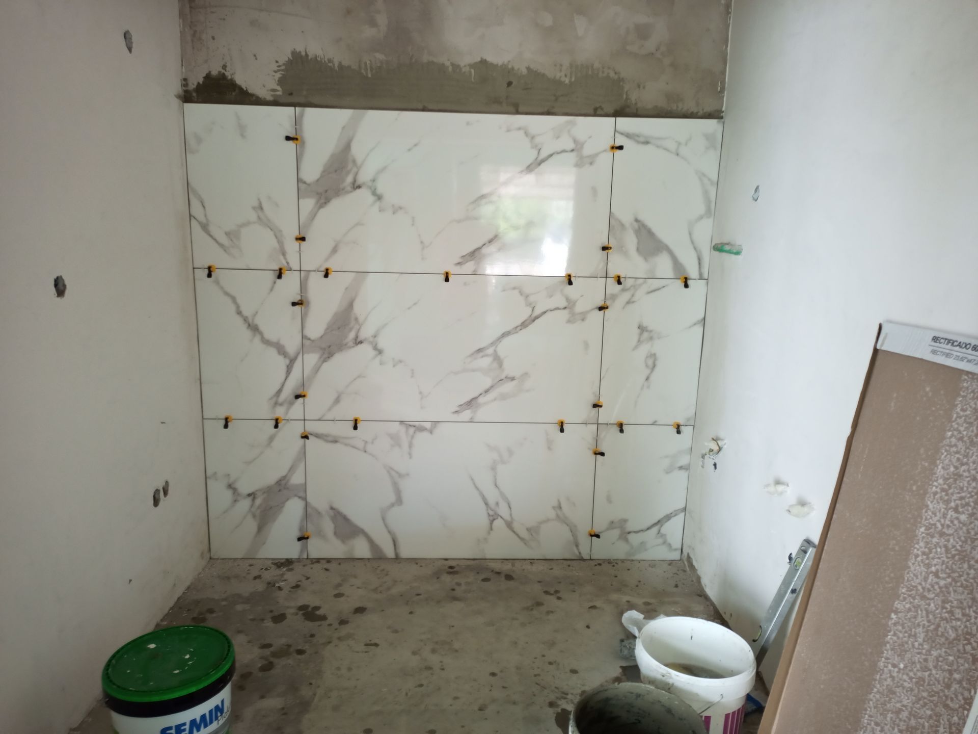 Parede do banheiro revestida com grandes azulejos brancos com estampa de mármore; espaçadores foram utilizados.