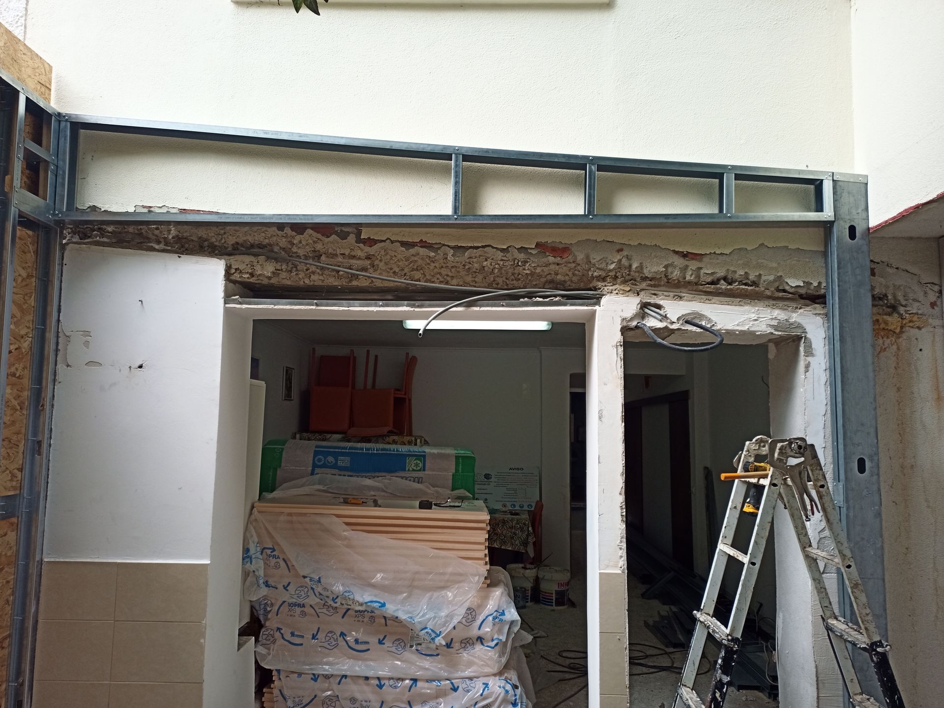 Canteiro de obras: porta com estrutura metálica, parede exposta, materiais no interior, escada próxima.