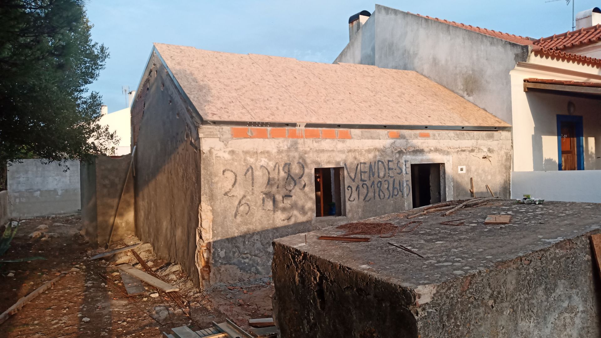 Pequeno prédio inacabado com telhado de telhas, tijolos aparentes e grafites na fachada.