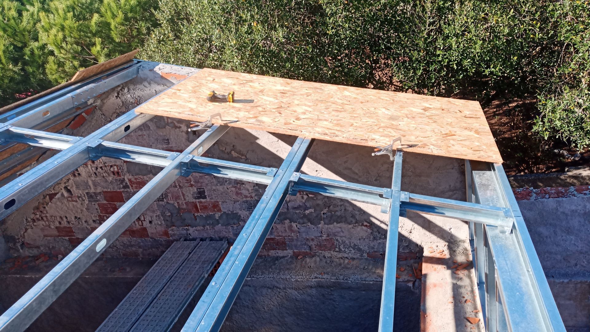 Estrutura metálica do telhado com compensado fixado, vista do interior da construção.