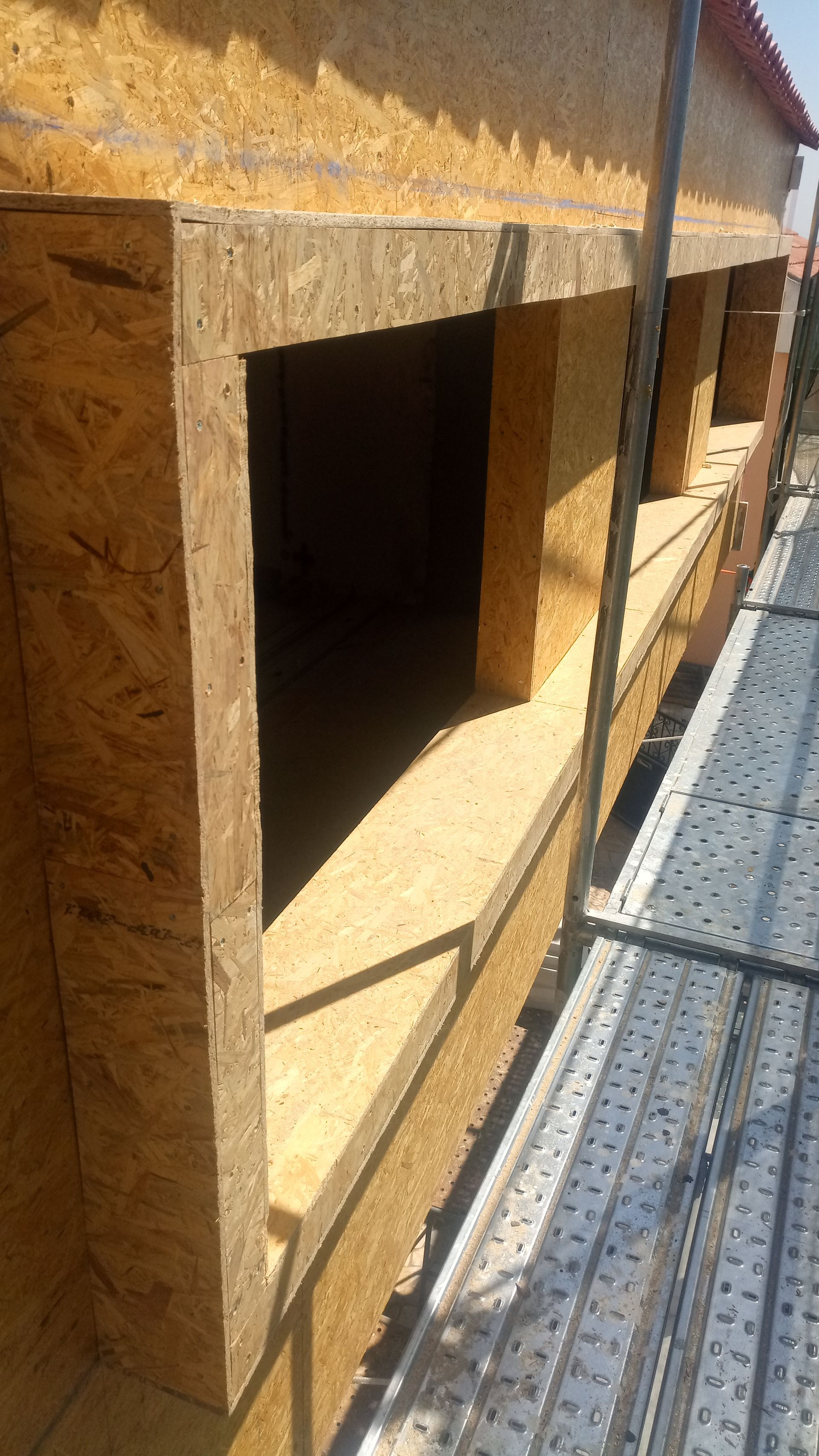 Construção em madeira OSB no exterior de um edifício, mostrando as molduras das janelas abertas e os andaimes.