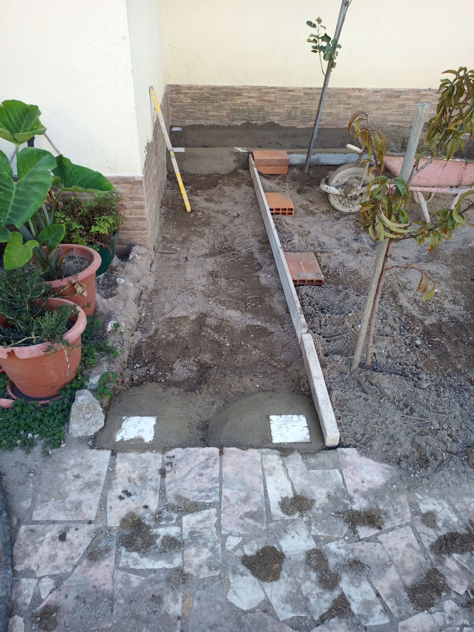Canteiro de obras: Base de concreto com tijolos e ferramentas em um pátio, ao lado de um prédio.