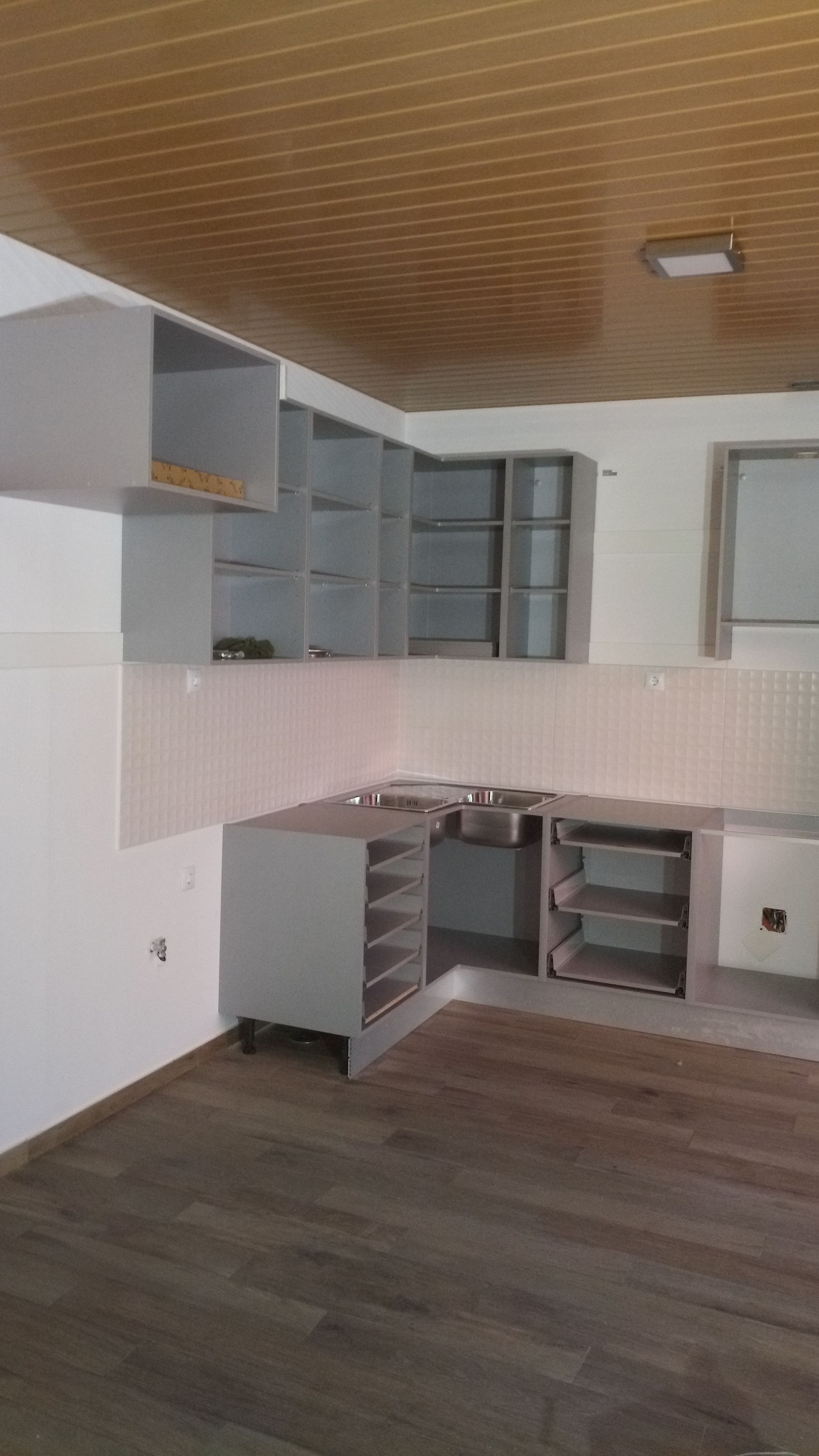 Cozinha com armários cinza, piso e teto de madeira, backsplash branco e pia.