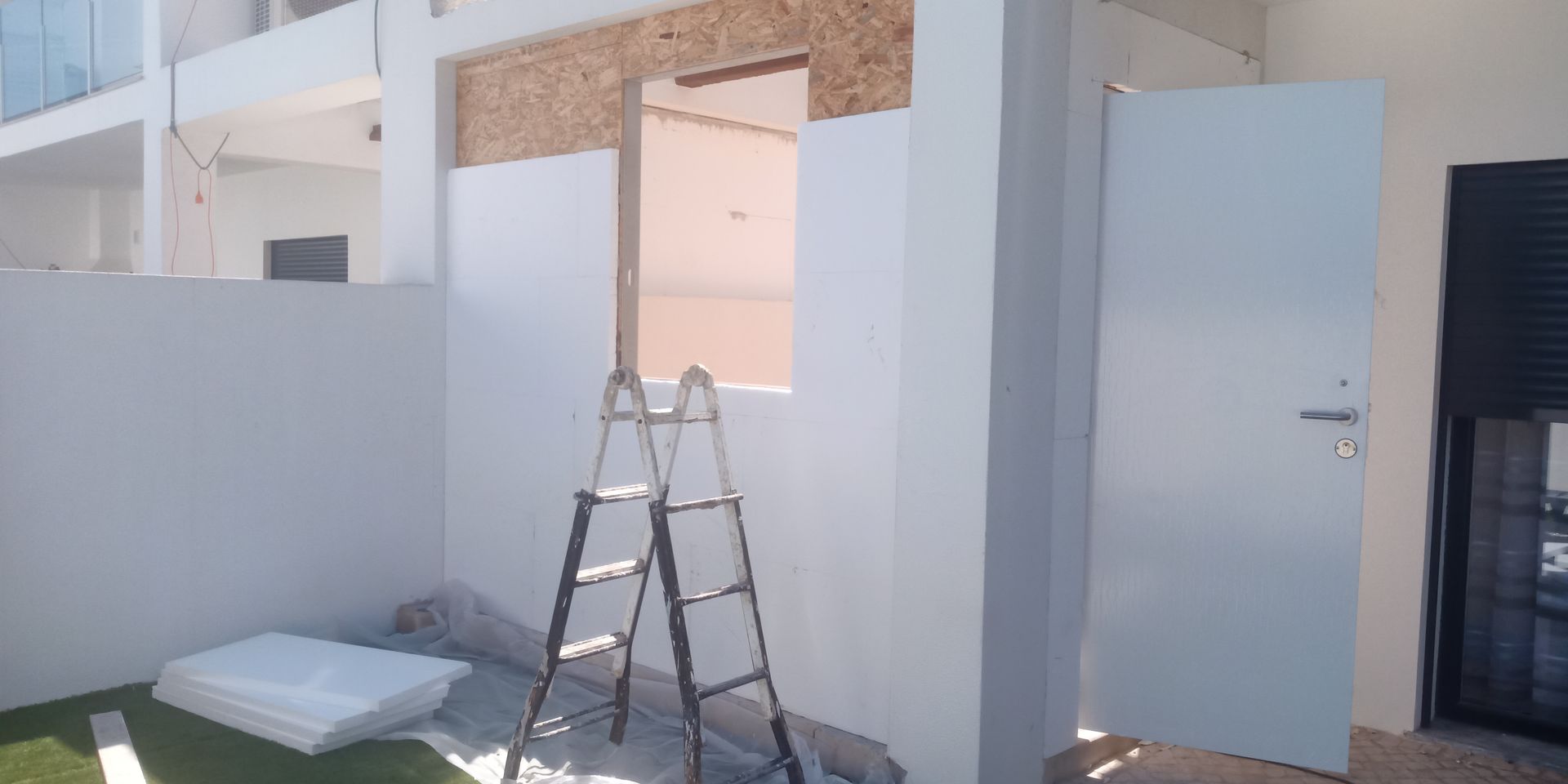Canteiro de obras com prédio inacabado, escada e porta aberta.