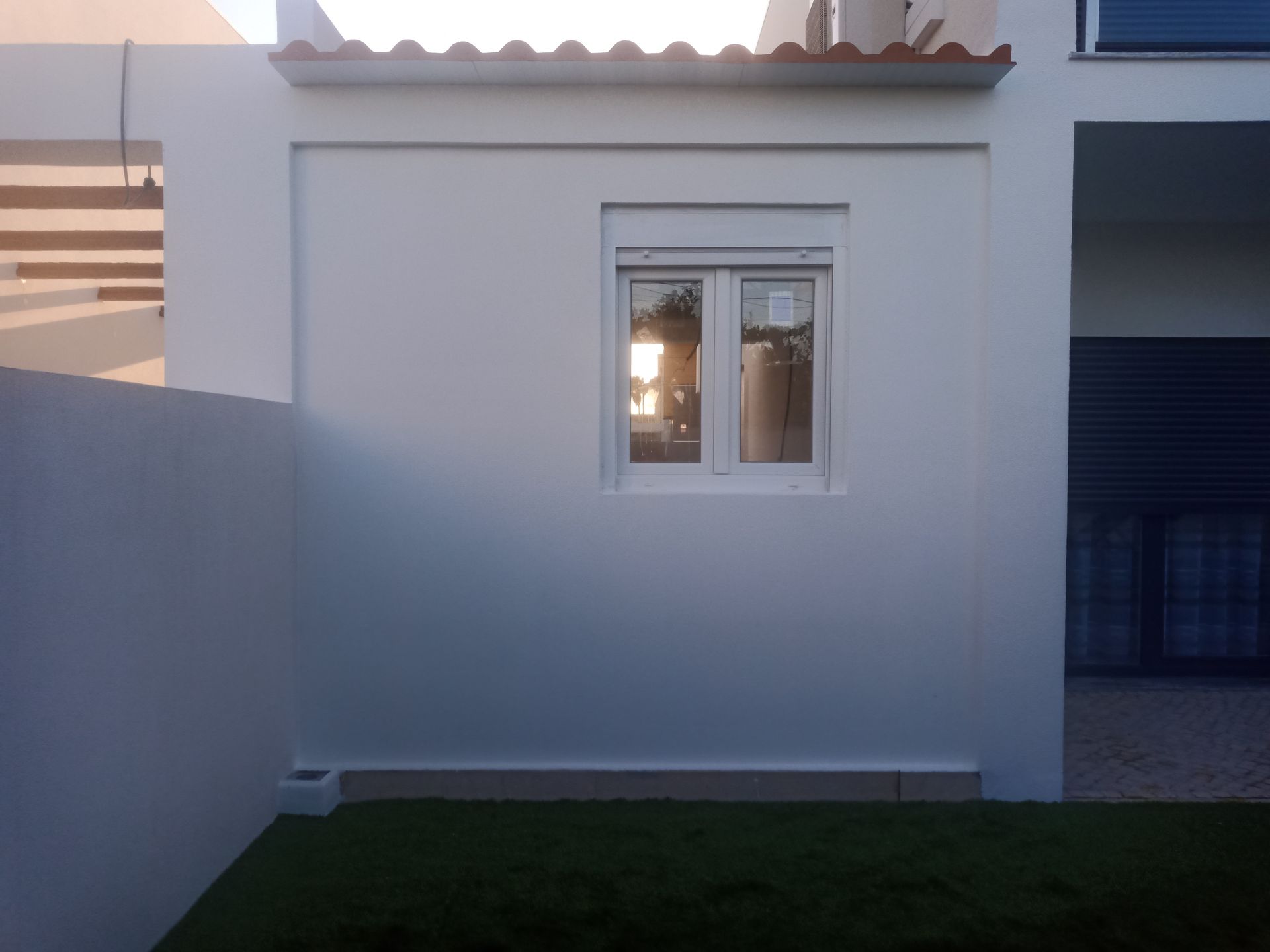 Prédio branco com uma janela e um pequeno telhado de telhas, contra um céu azul, com um pouco de grama verde na frente.