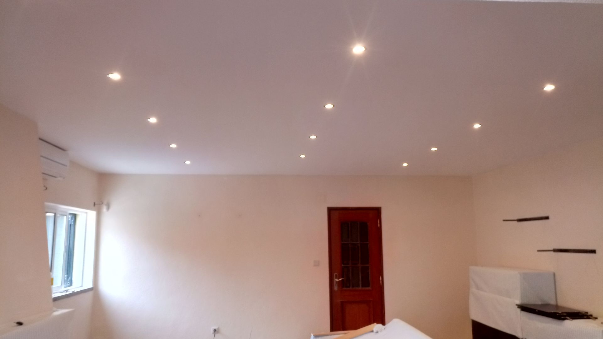 Quarto com teto branco, iluminação embutida, porta, janela e paredes cor creme.