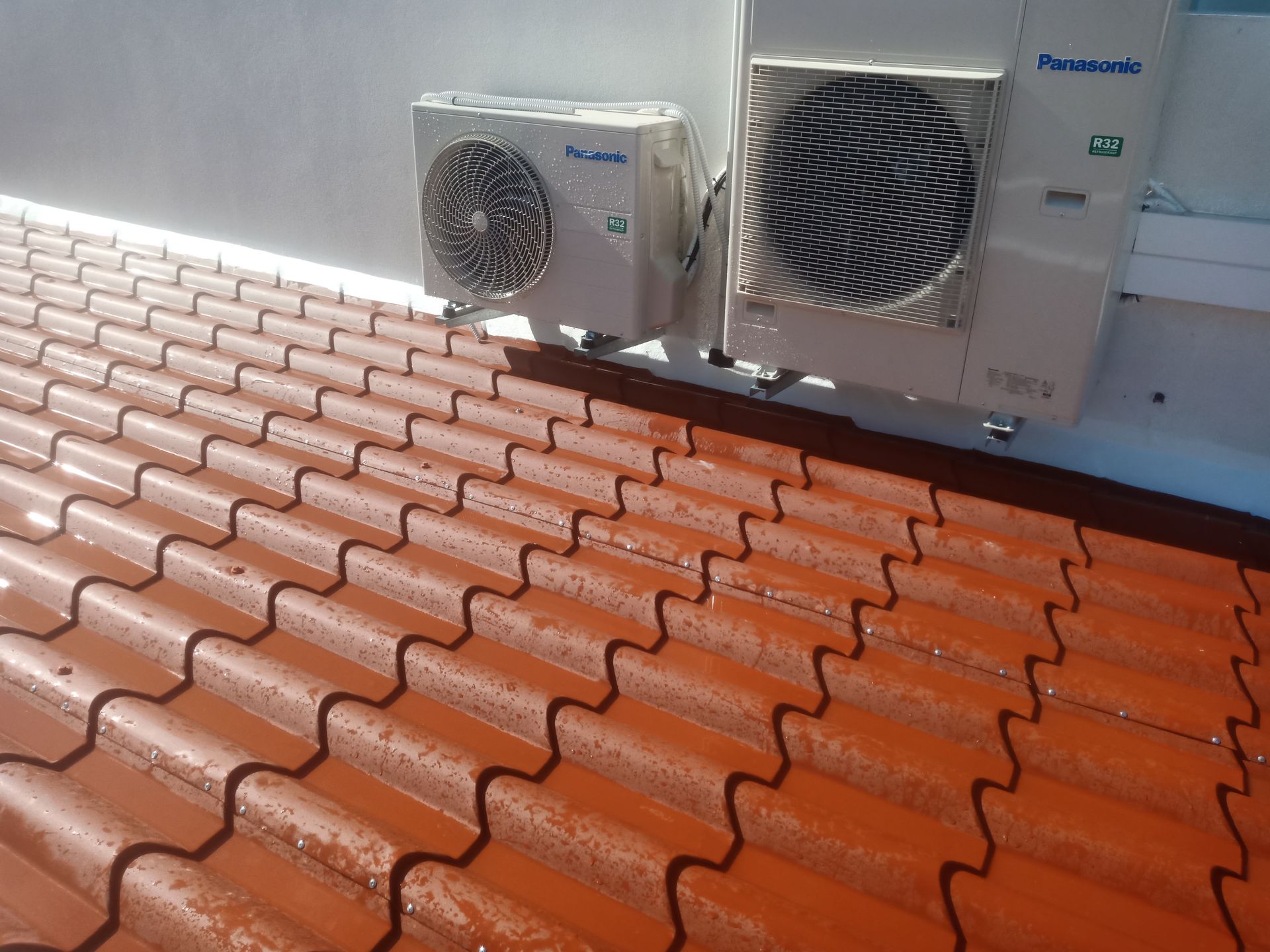 Duas unidades de ar condicionado Panasonic instaladas em um telhado de telhas vermelhas, contra uma parede branca.