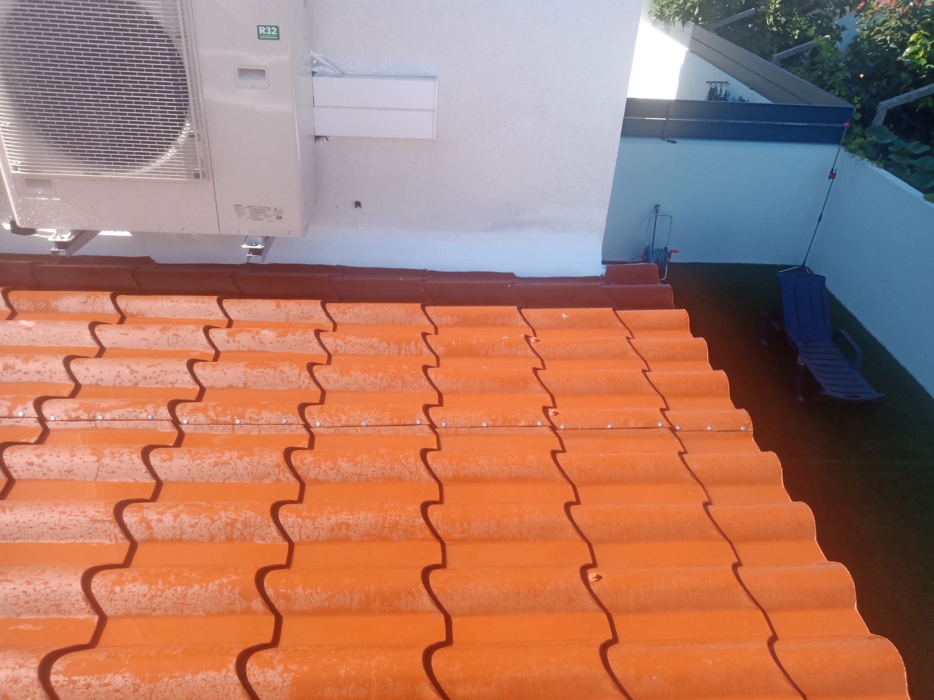 Telhado de telhas laranja com aparelho de ar condicionado encostado em uma parede branca.
