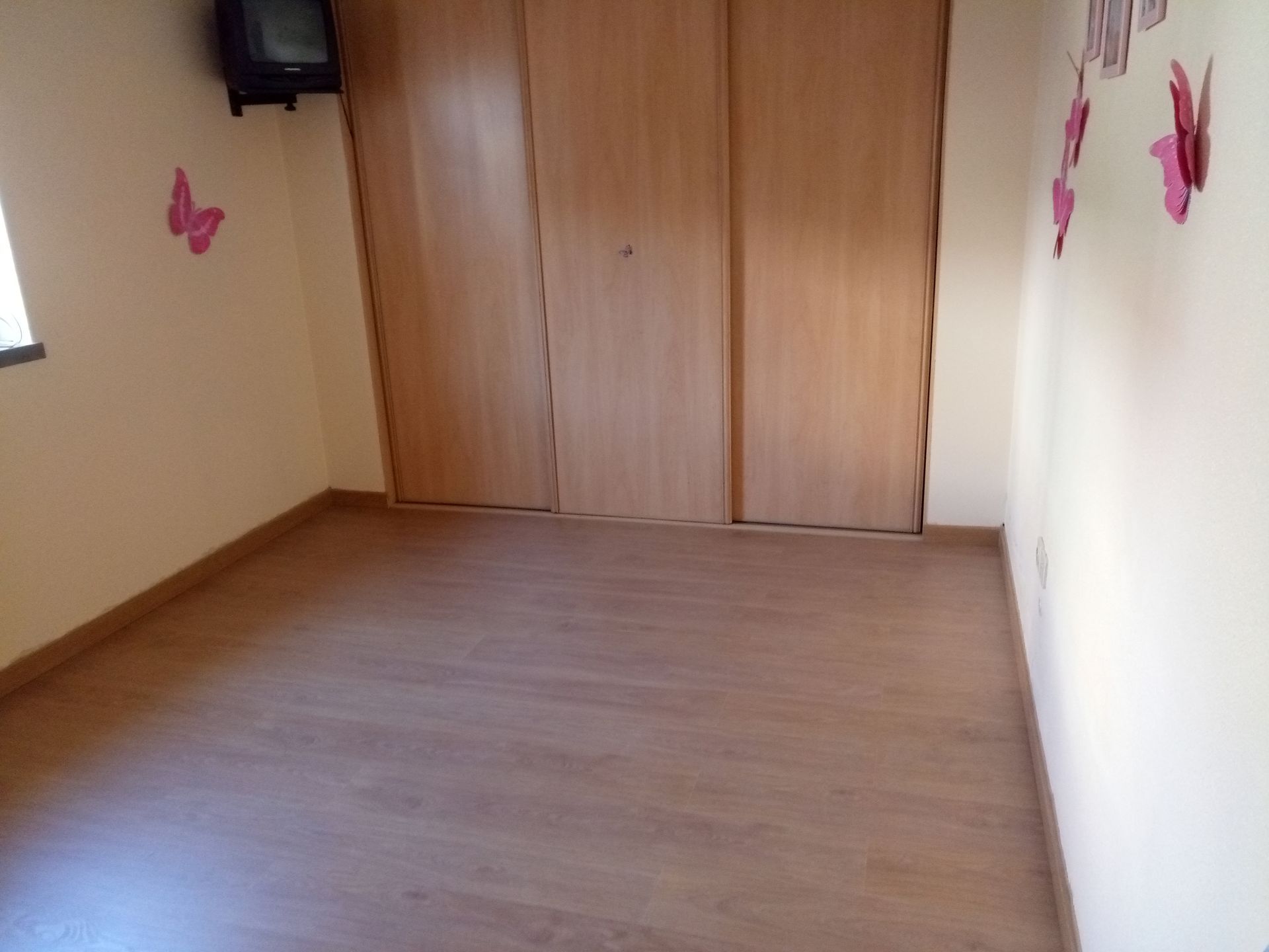Quarto vazio com piso de madeira, armário, TV e adesivos de parede de borboletas.