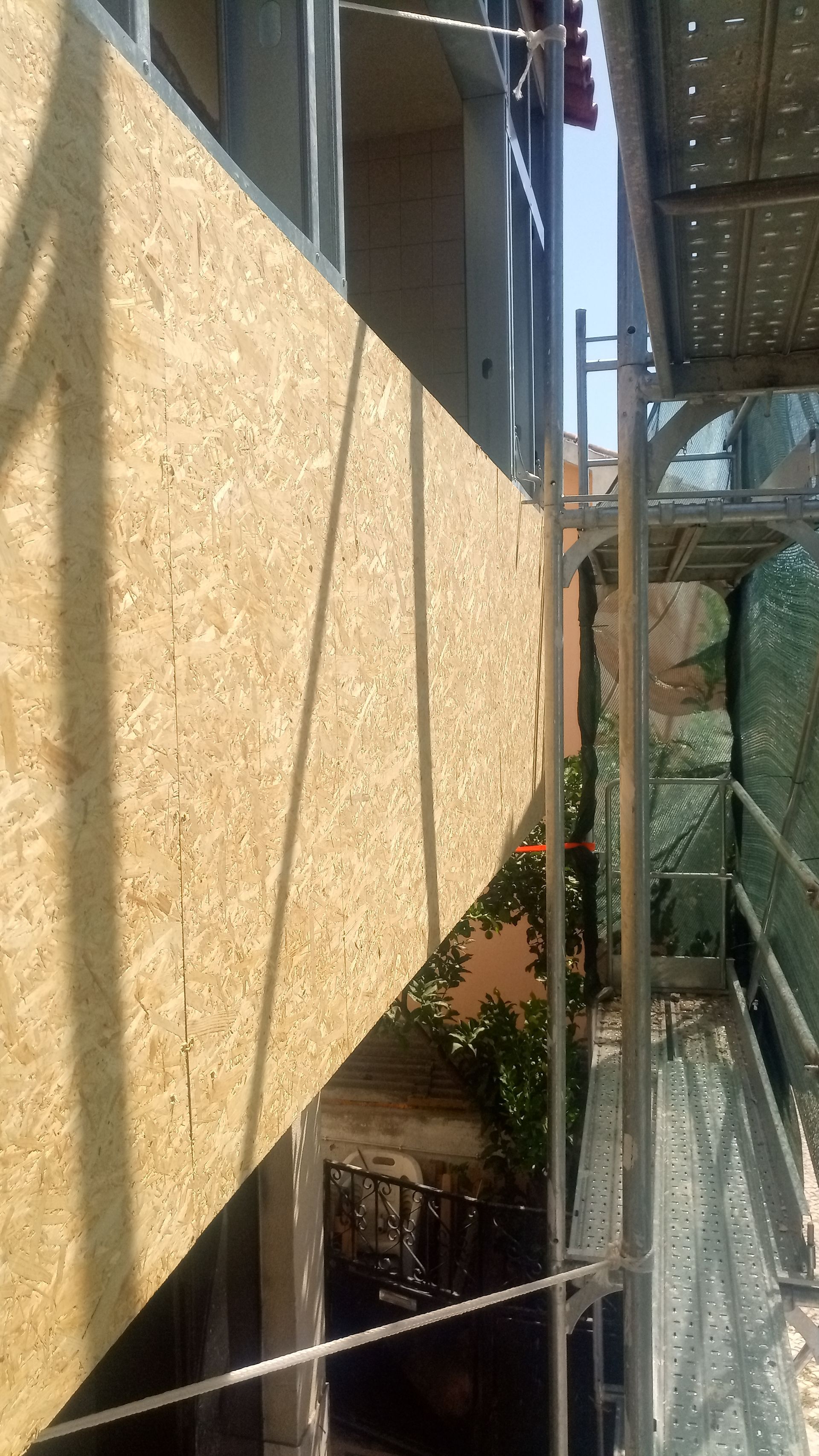 Andaimes de construção ao lado da parede de um edifício com painéis de madeira.