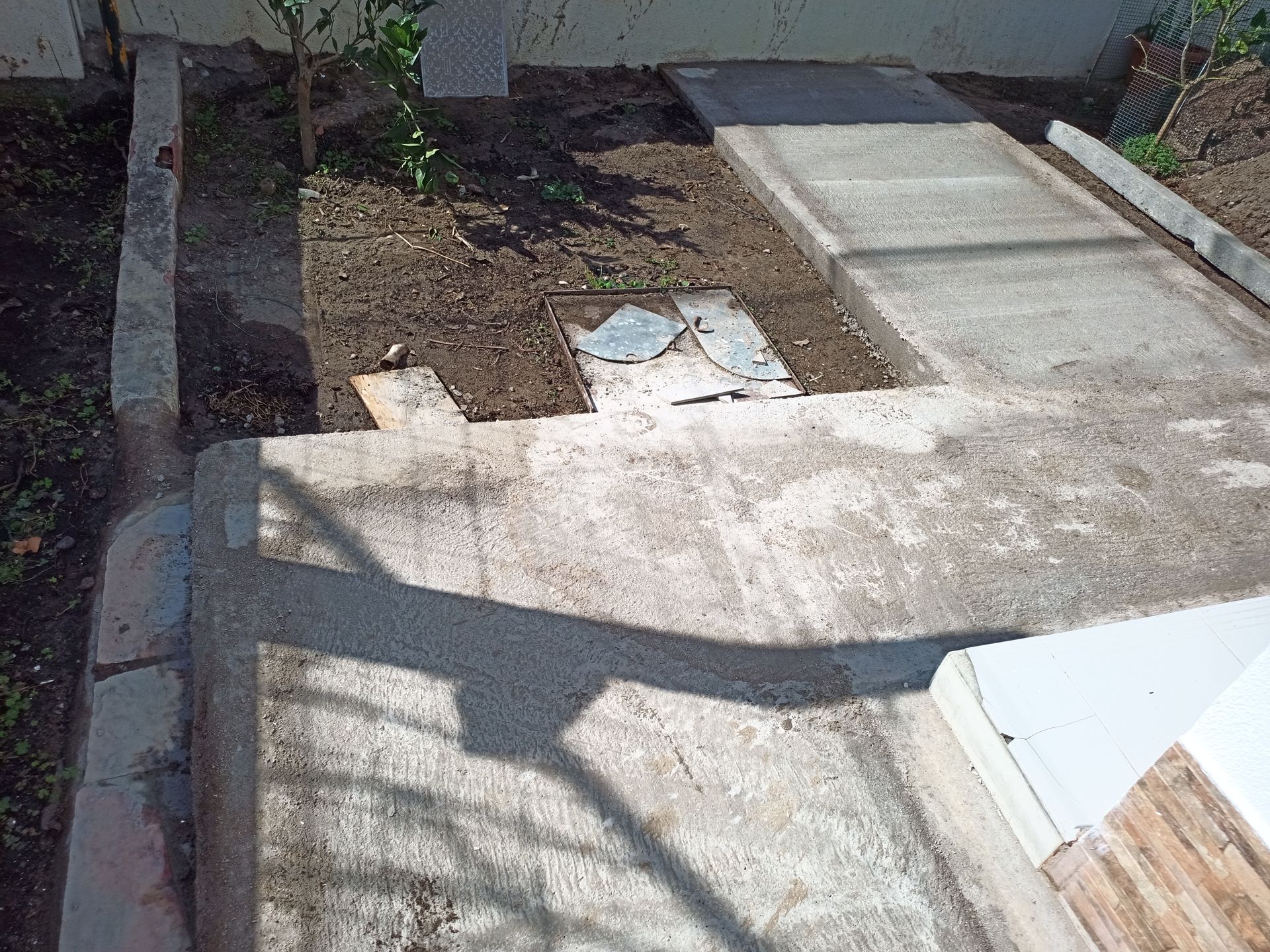 Caminho de concreto e canteiro de jardim, parte de uma passarela com um painel de acesso quadrado visível.
