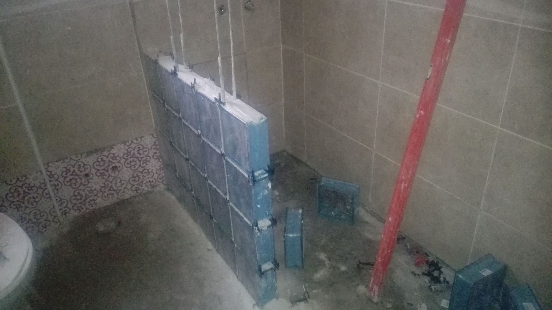Banheiro em construção com paredes parcialmente revestidas com azulejos e nivelado.