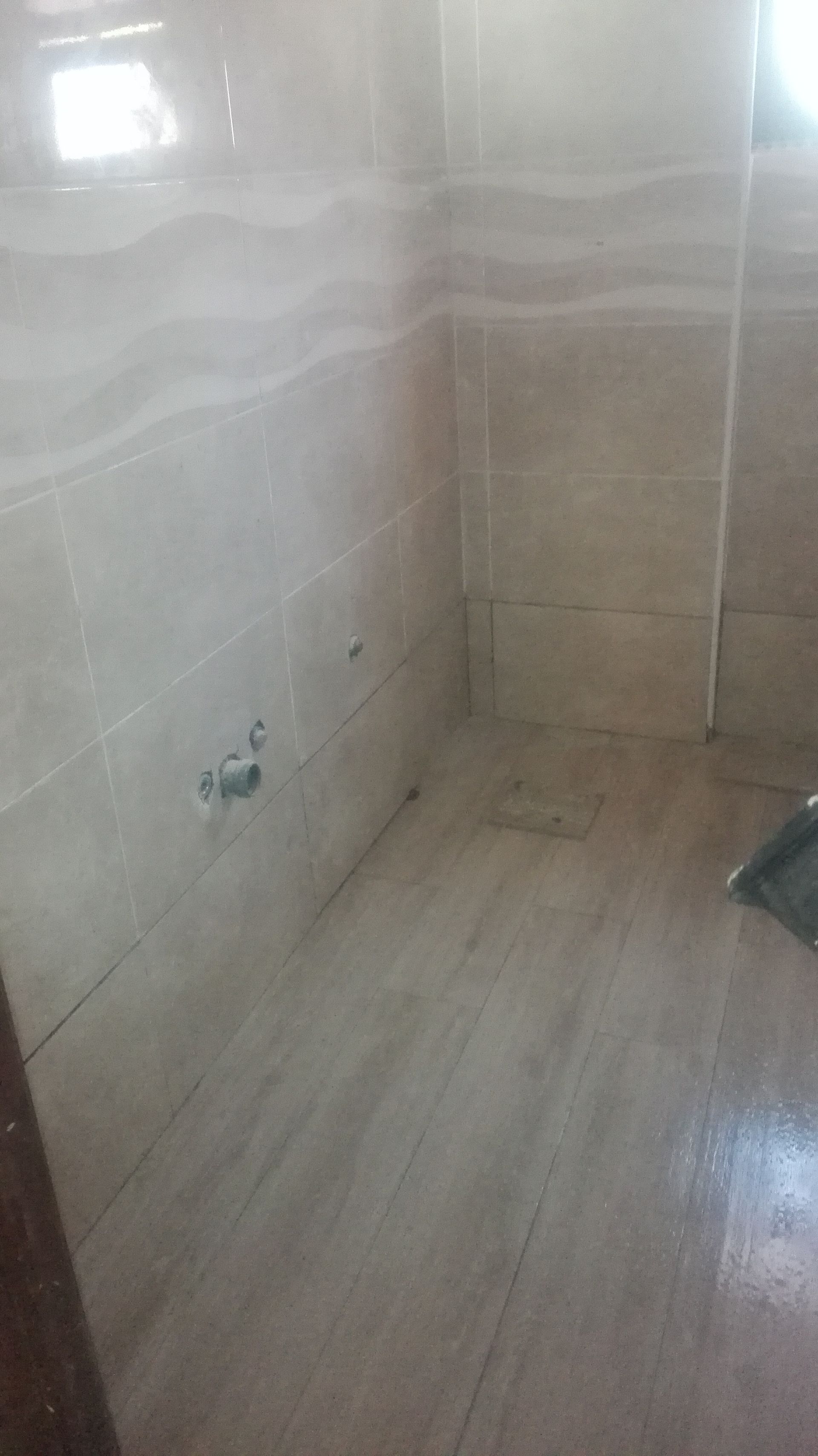 Banheiro vazio com paredes e piso revestidos com azulejos claros. Uma janela quadrada é visível no canto superior esquerdo.