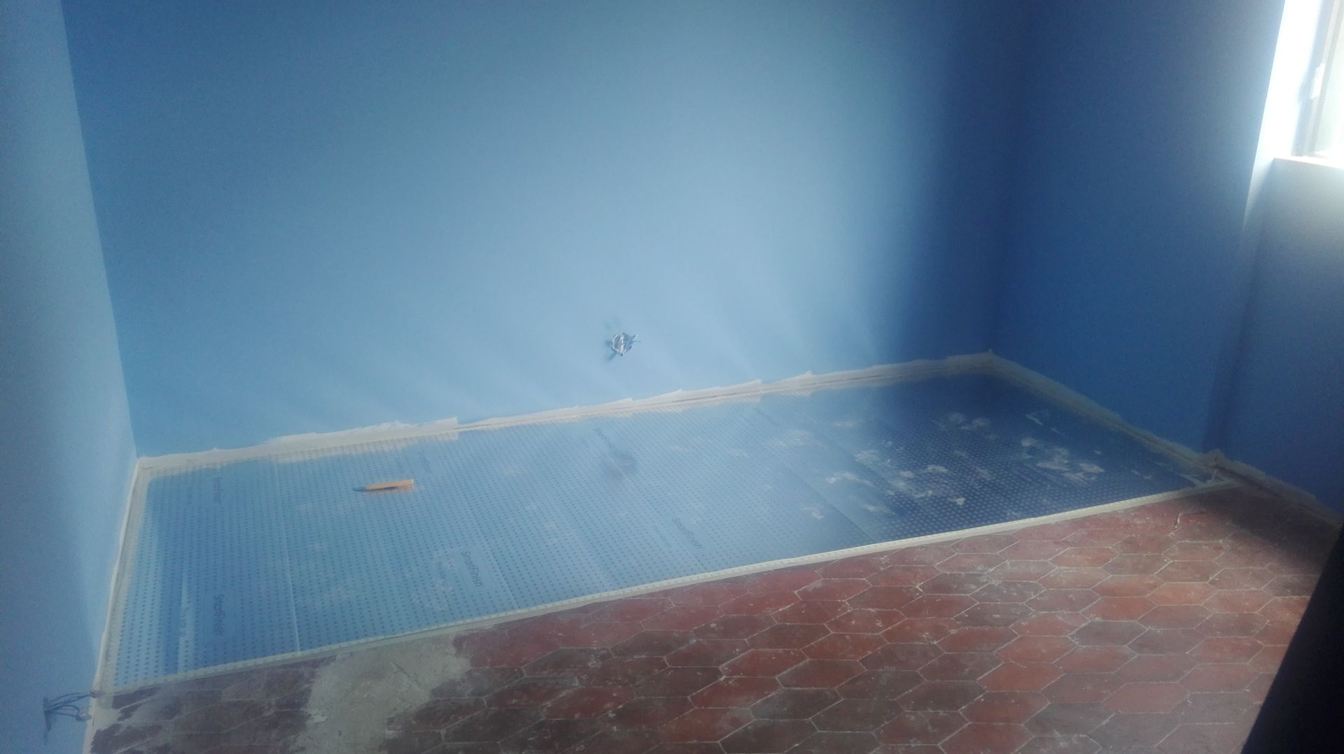 Quarto azul vazio com chão molhado e azulejos vermelhos manchados.