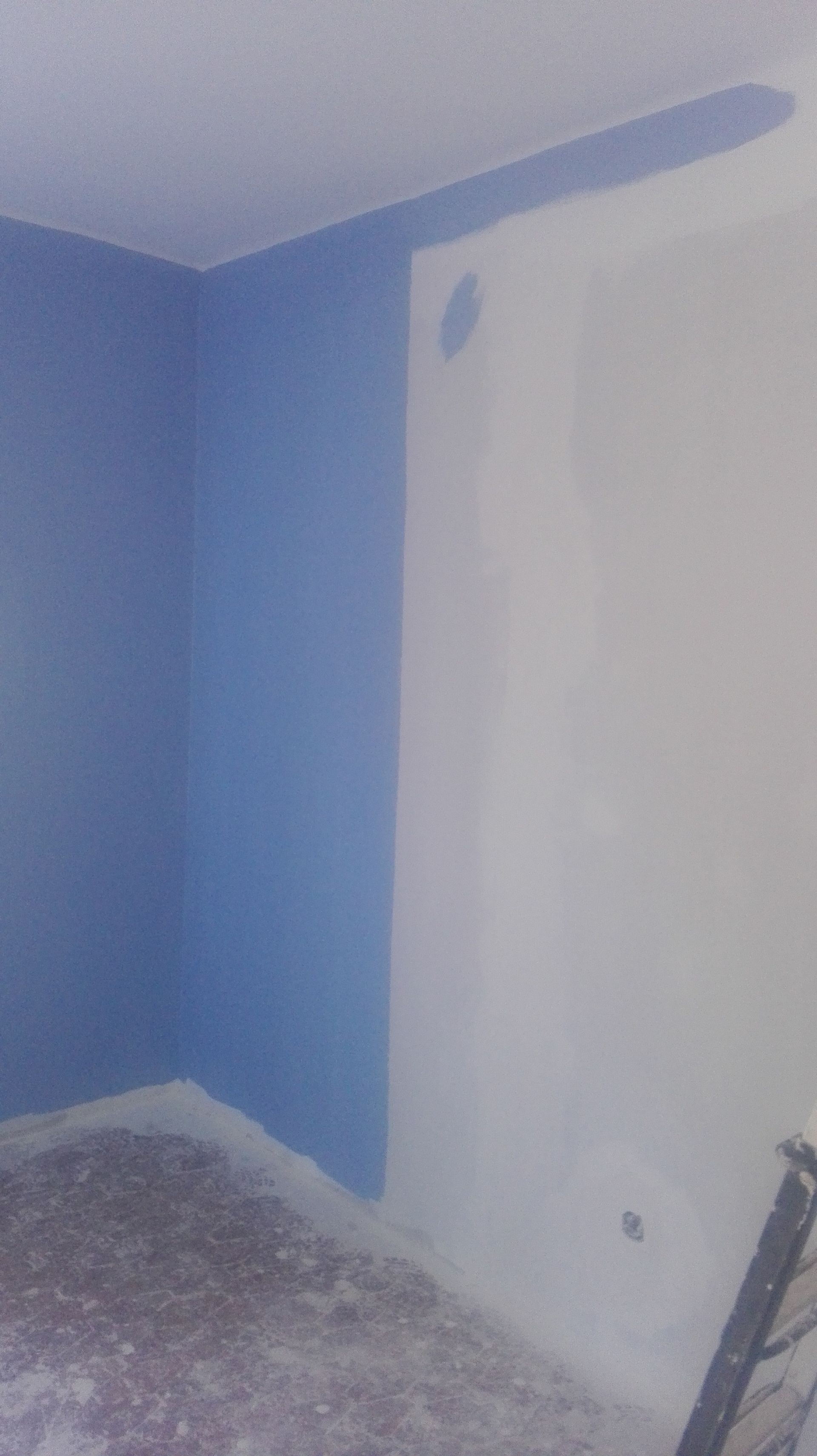 Canto de parede pintado de azul ao lado de uma parede branca, em um cômodo inacabado.