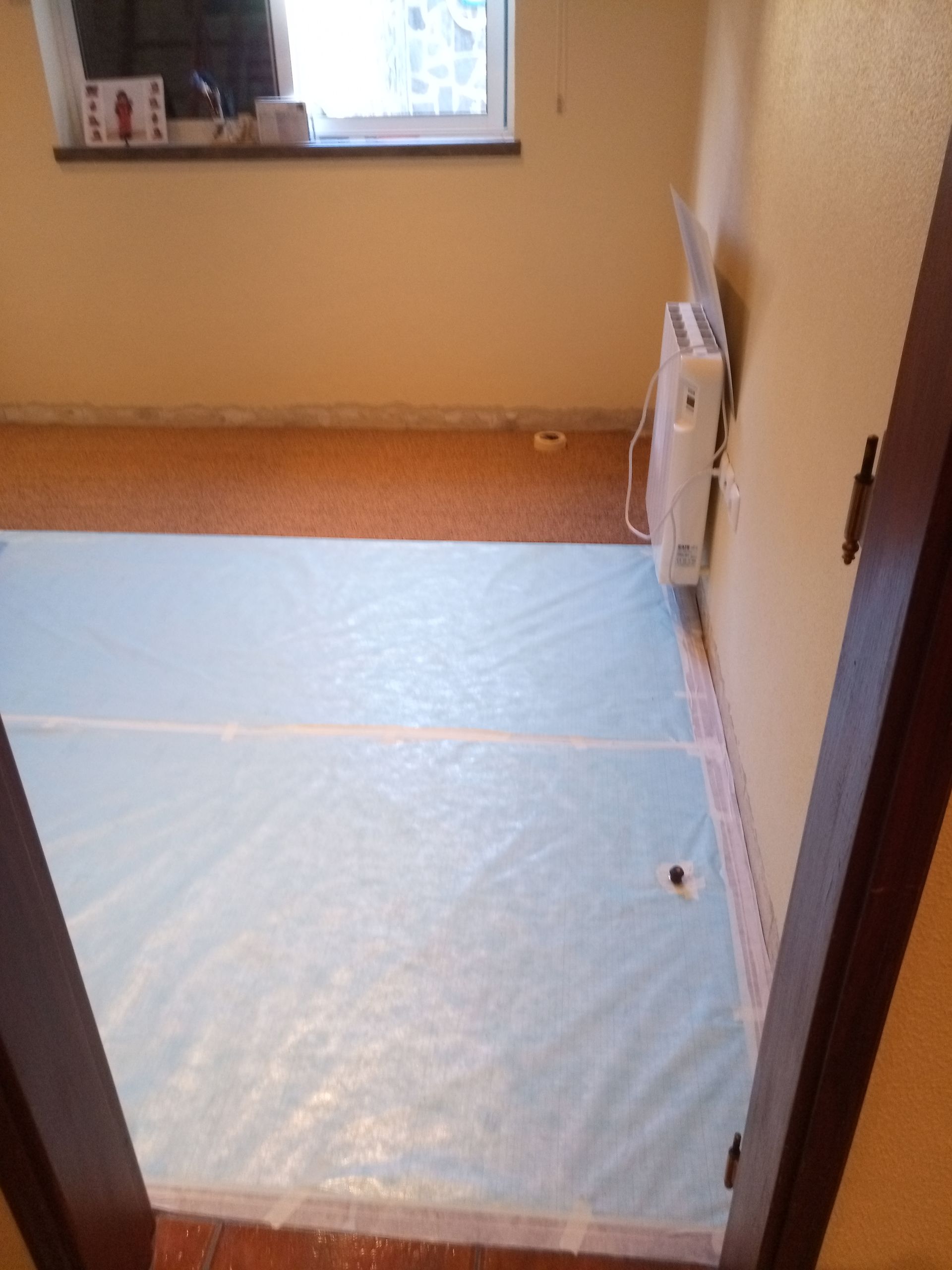 Quarto com piso revestido em azul claro e aquecedor de parede próximo a uma janela.