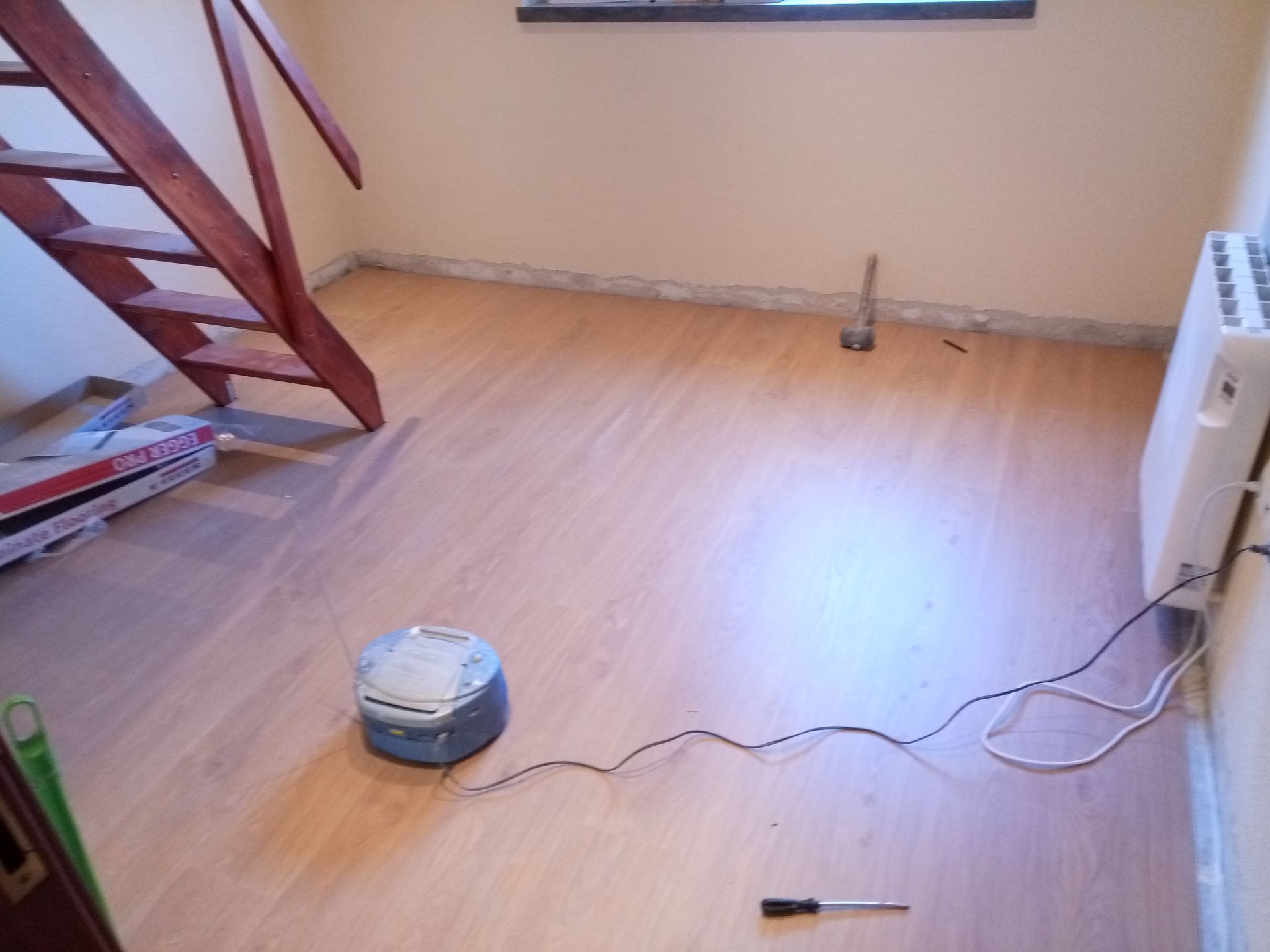 Quarto com piso de madeira, escadas, aquecedor e ferramentas.