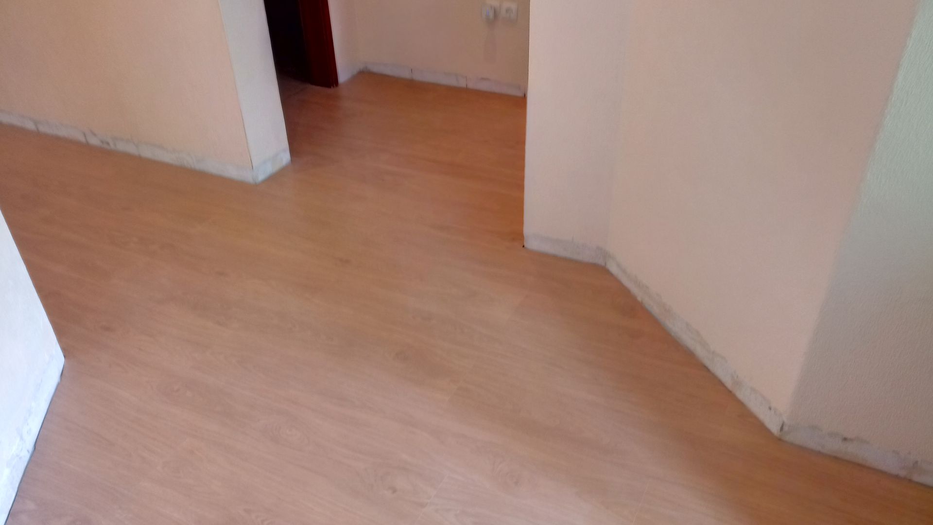 Piso de madeira em um corredor com paredes cor de pêssego e uma porta ao fundo.