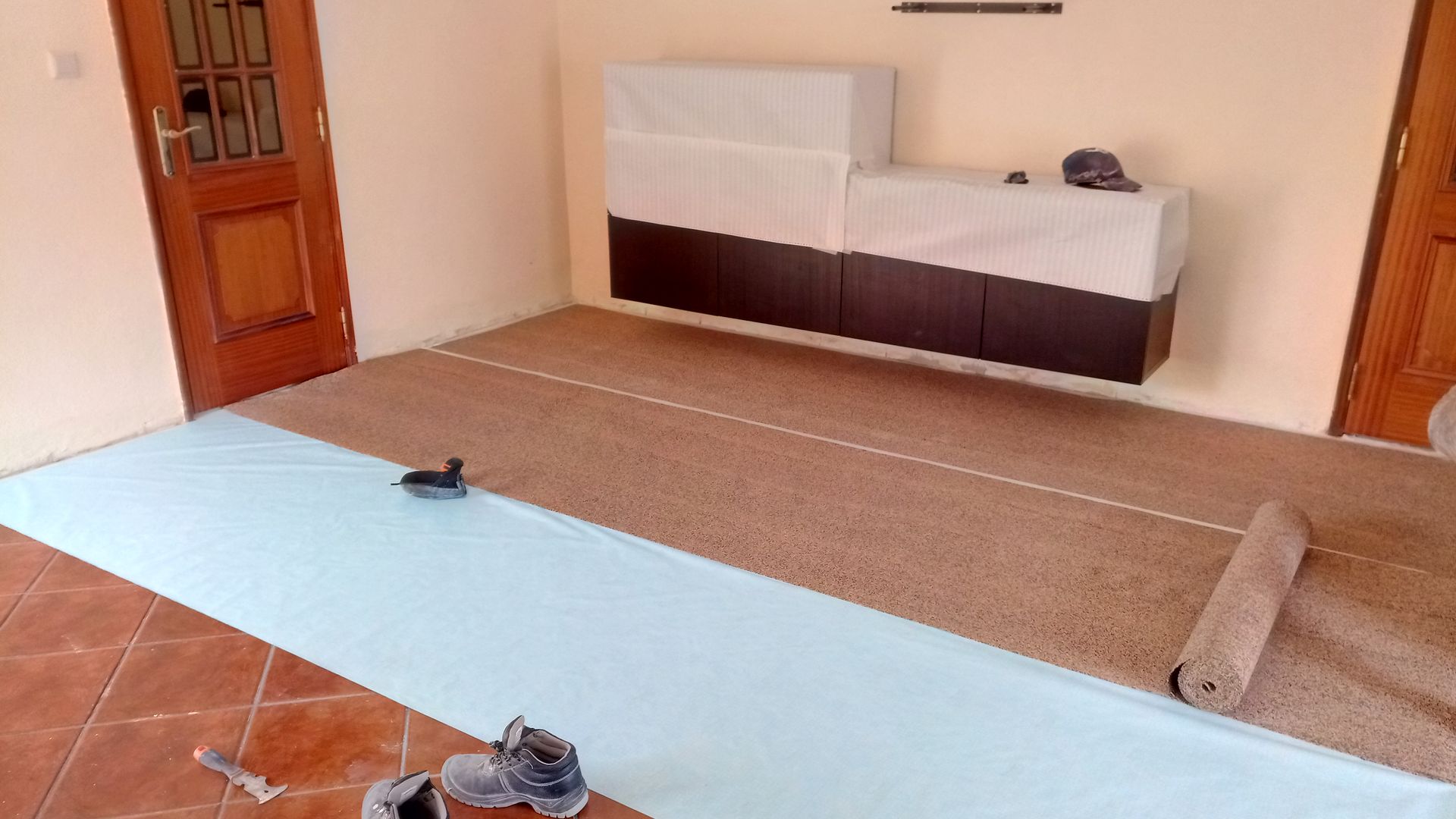 Quarto com piso em processo de instalação; carpete marrom sendo desenrolado sobre base azul, armários na parede.