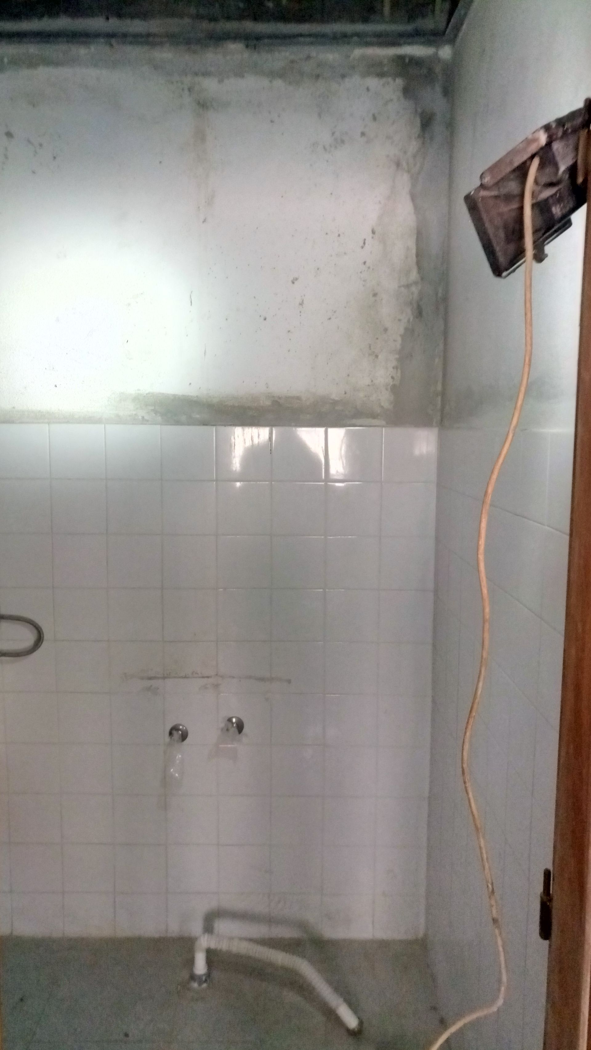 Parede do banheiro revestida com azulejos brancos, com mofo e luminária com fio.