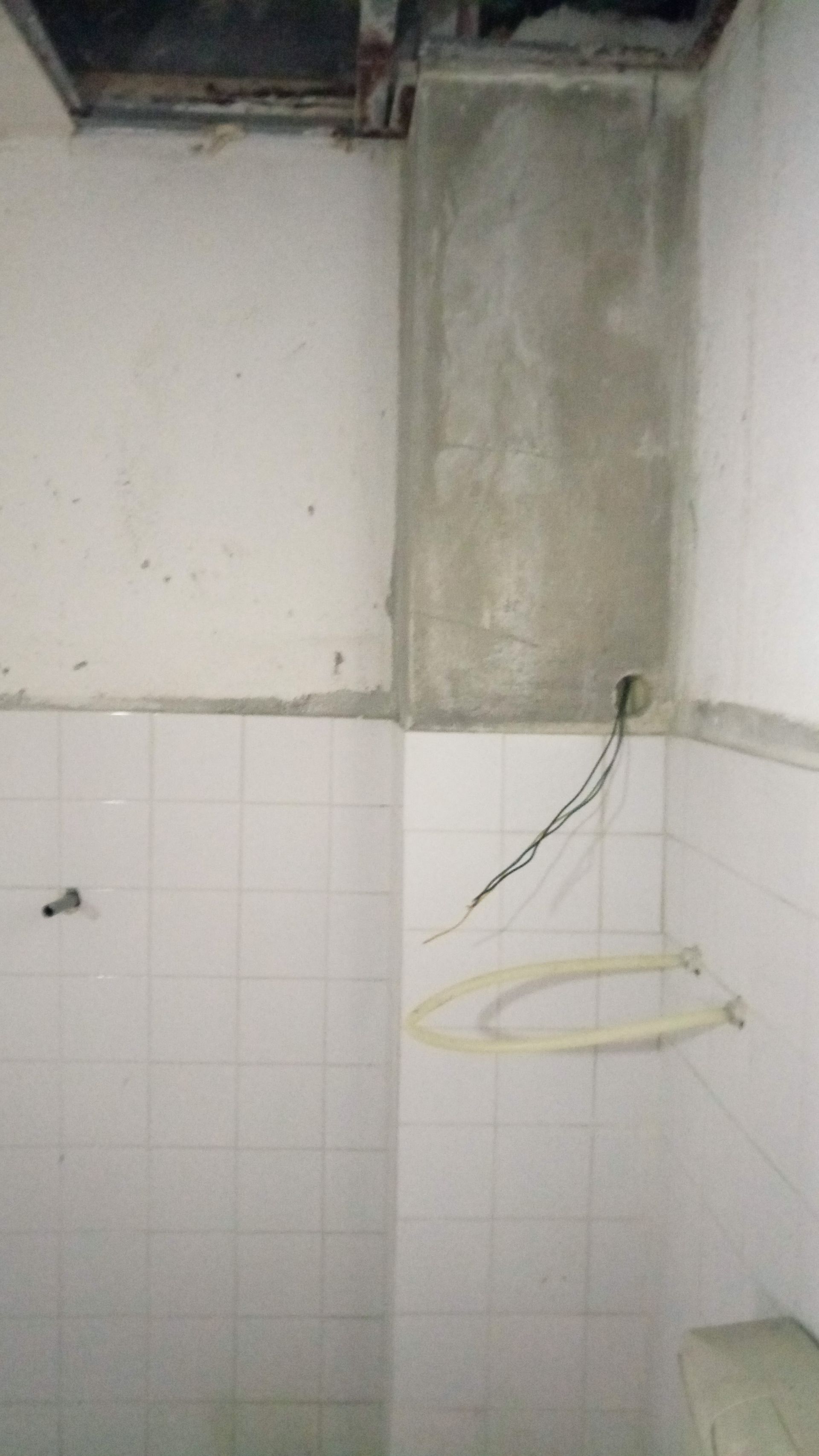 Banheiro em construção com paredes inferiores revestidas com azulejos brancos, seção de cimento aparente e fiação exposta.