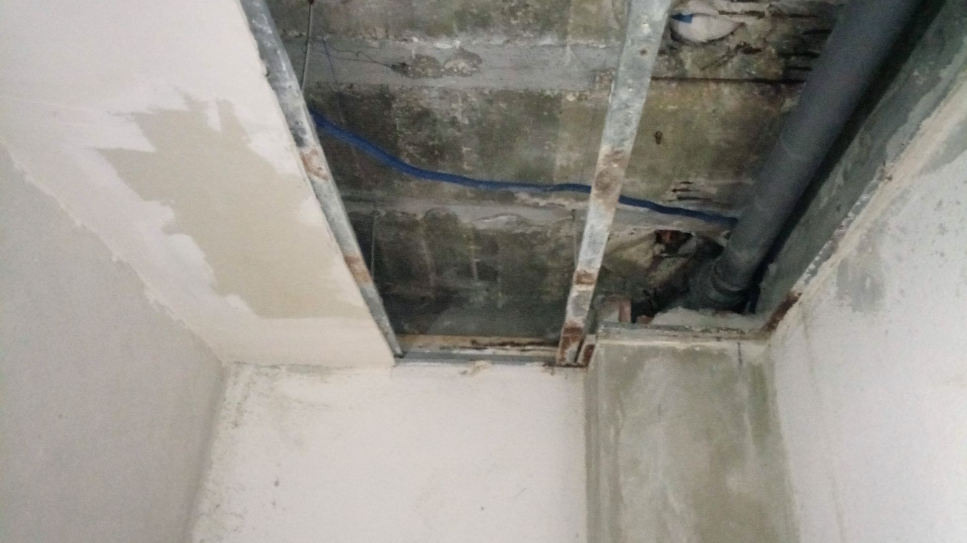 Teto aparente com tubulações e vigas, construção inacabada.