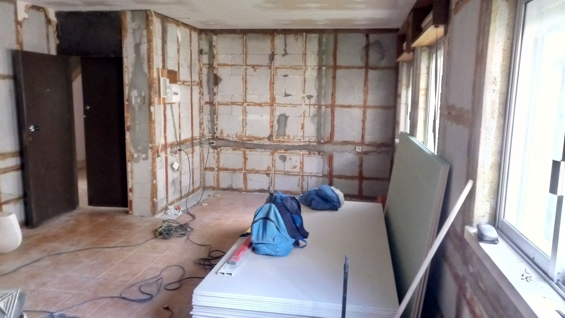 Interior em reforma; vigas de parede expostas, colchão, drywall, porta e janelas.