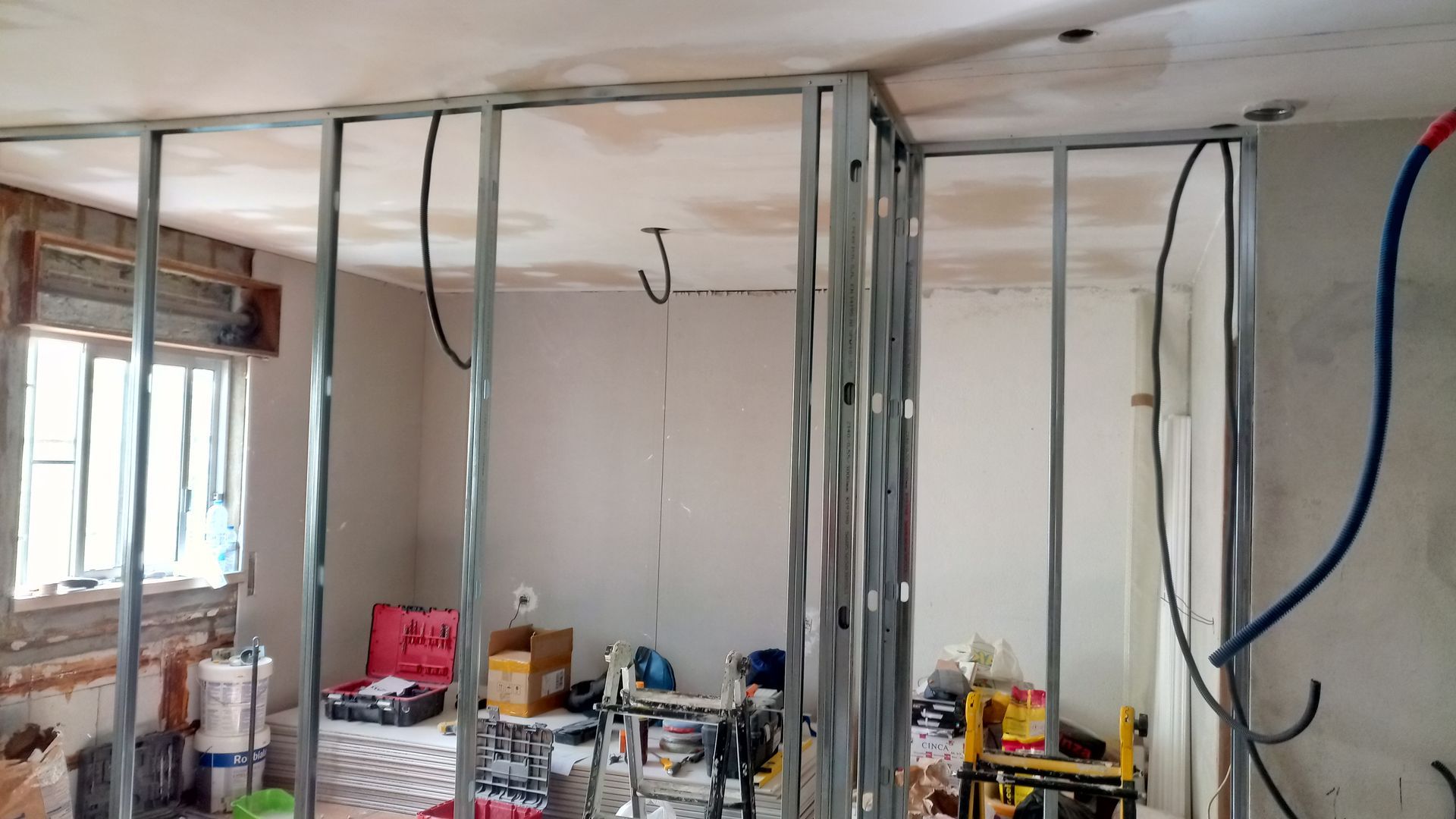 Interior de um cômodo em construção; estrutura de metal já instalada para as paredes e o teto.