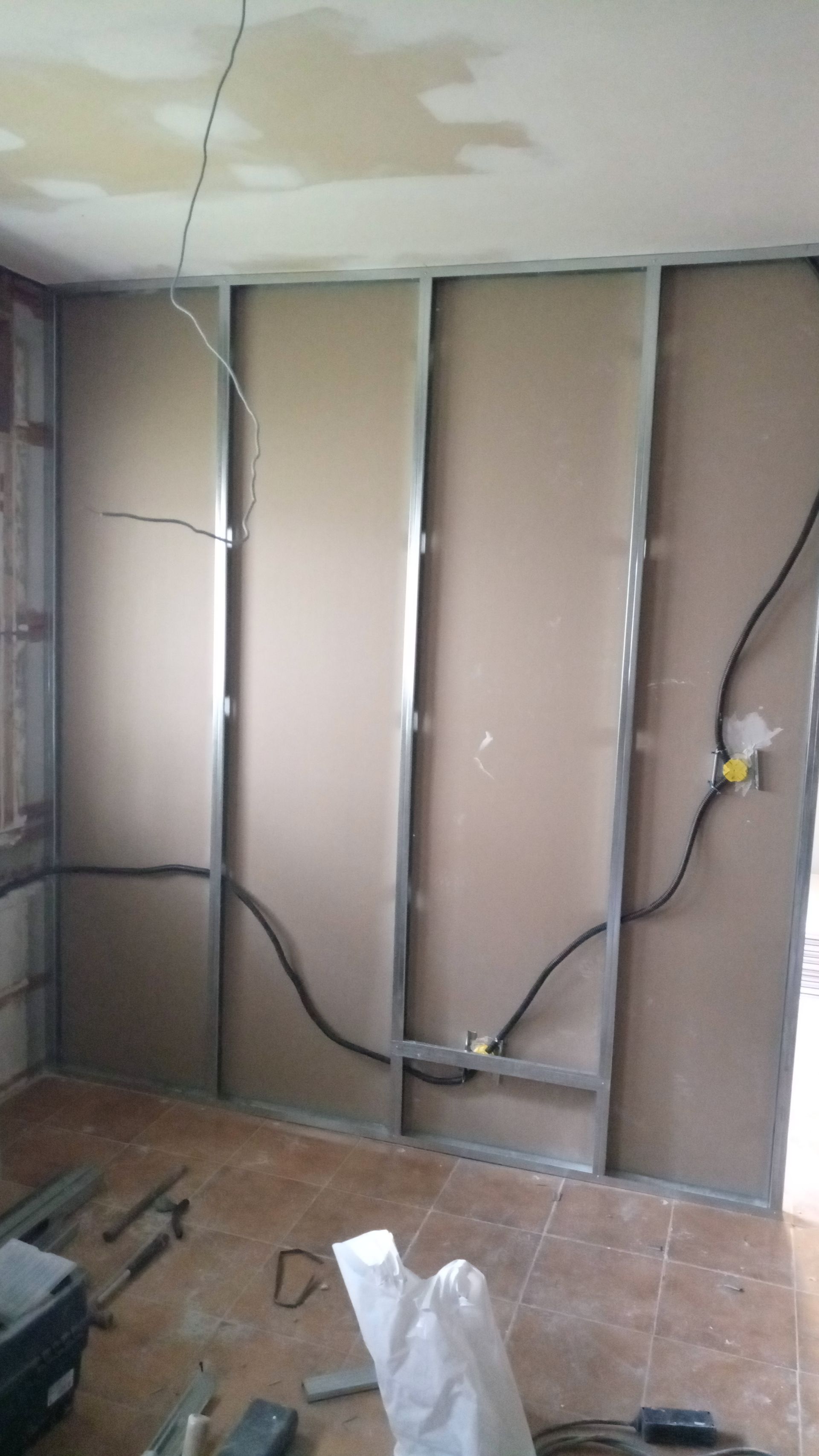 Construção da parede interna: estrutura metálica com drywall, fiação elétrica aparente. O piso do cômodo é de cerâmica.