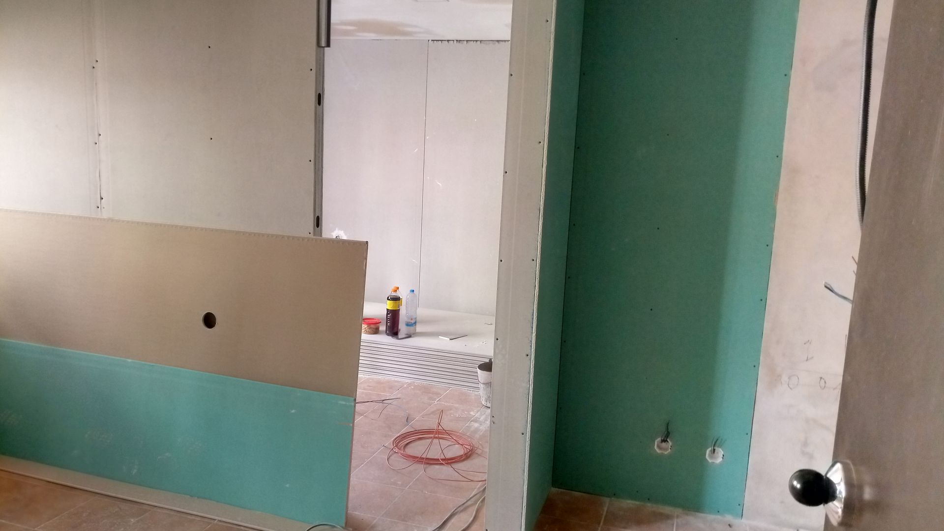 Interior em reforma com drywall aparente, paredes e portas em tons de verde e bege.