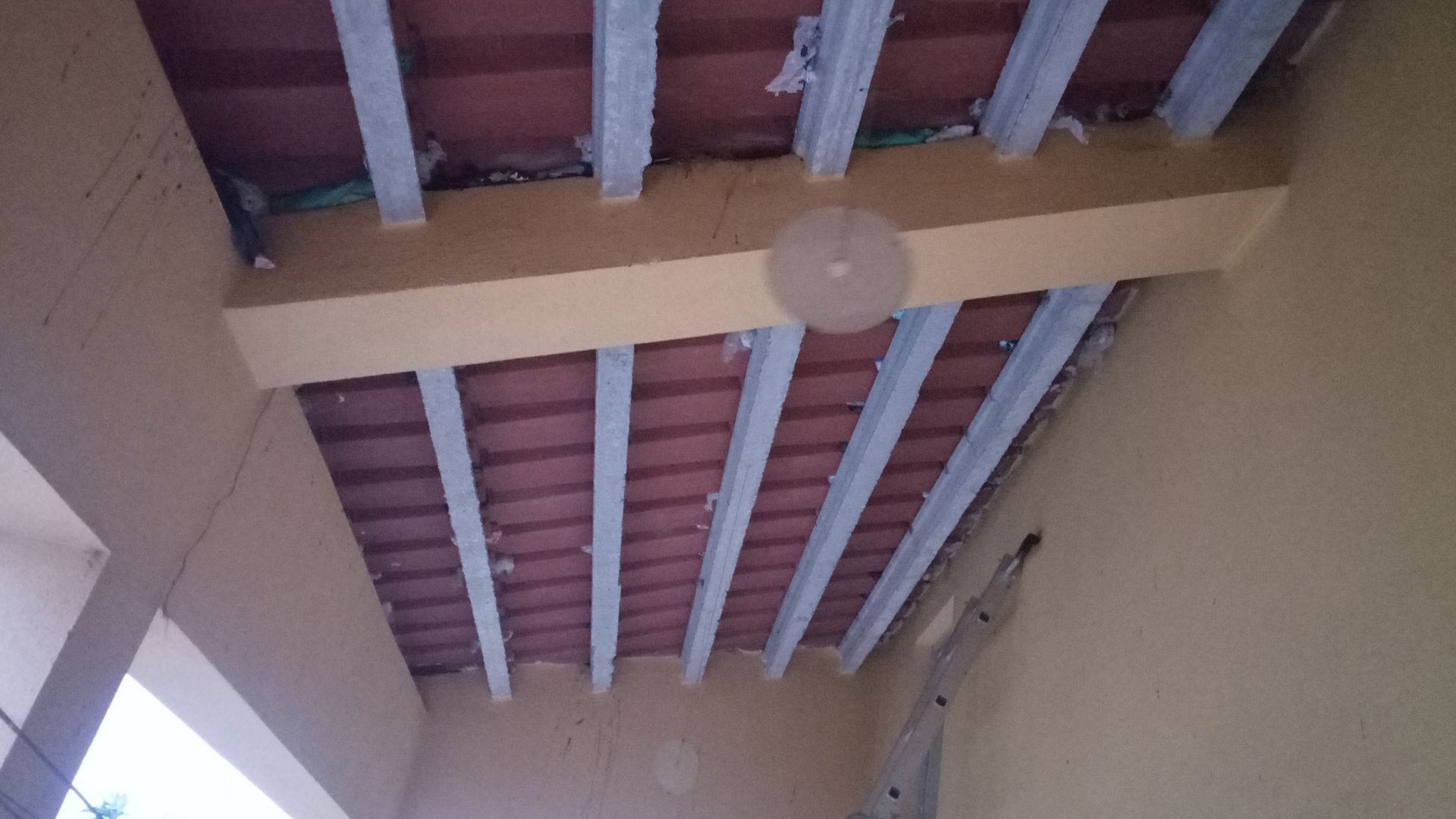 Vista de um teto parcialmente construído com telhas de terracota, vigas e suportes metálicos.