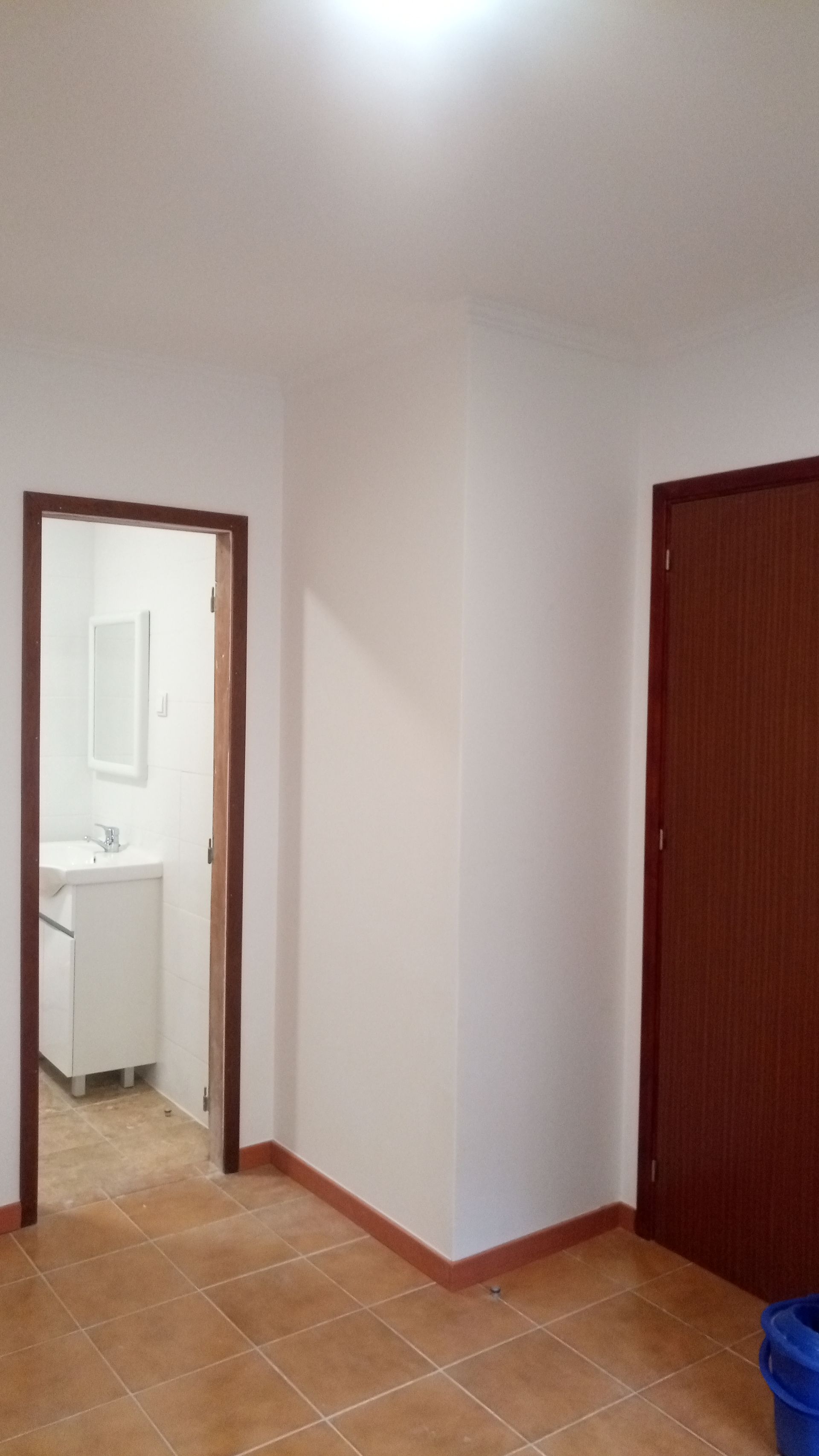 Um quarto com porta de banheiro e porta marrom. Paredes brancas com detalhes em marrom e piso de azulejo.