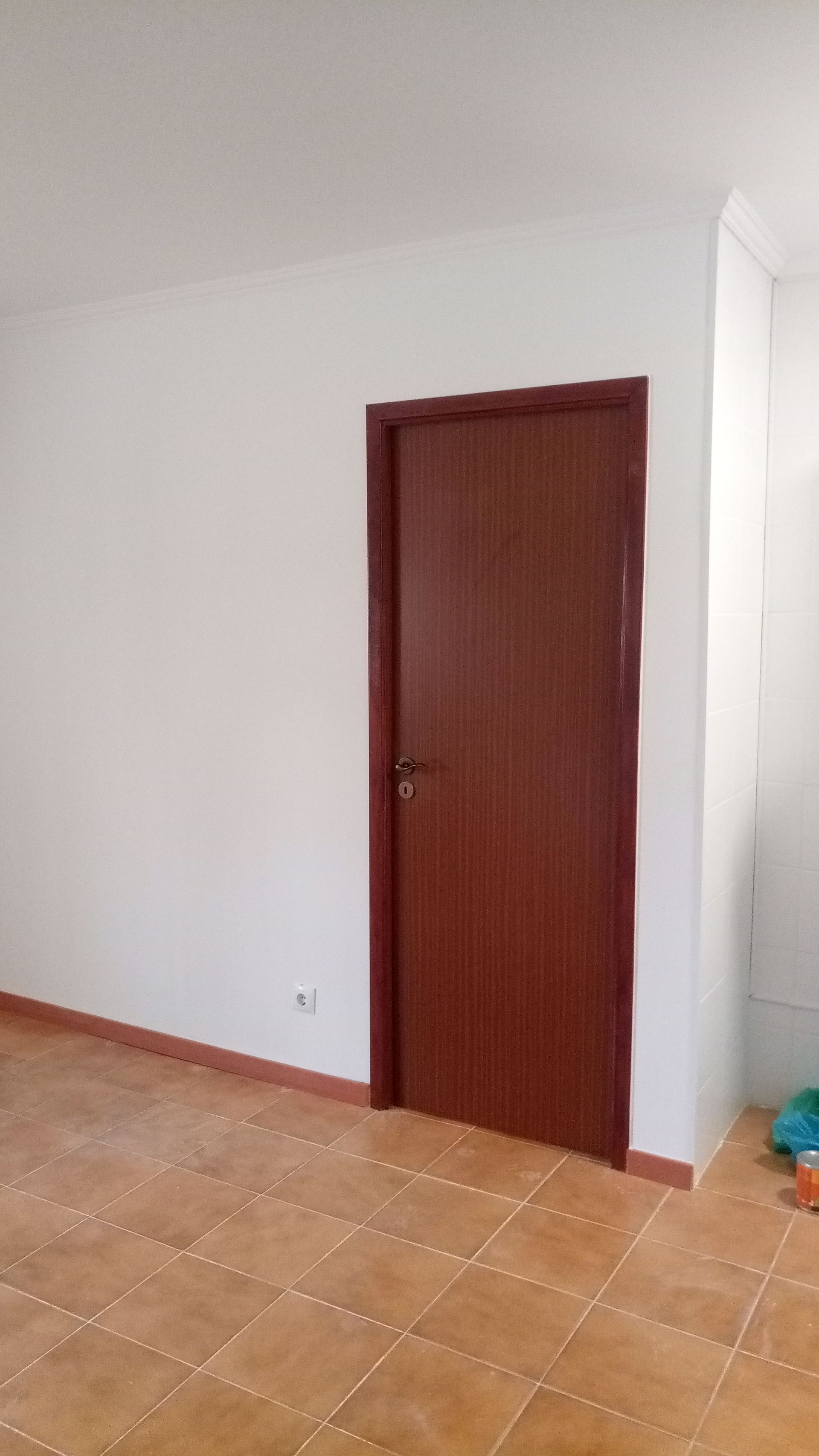 Porta marrom em um quarto com paredes brancas e piso de azulejo.