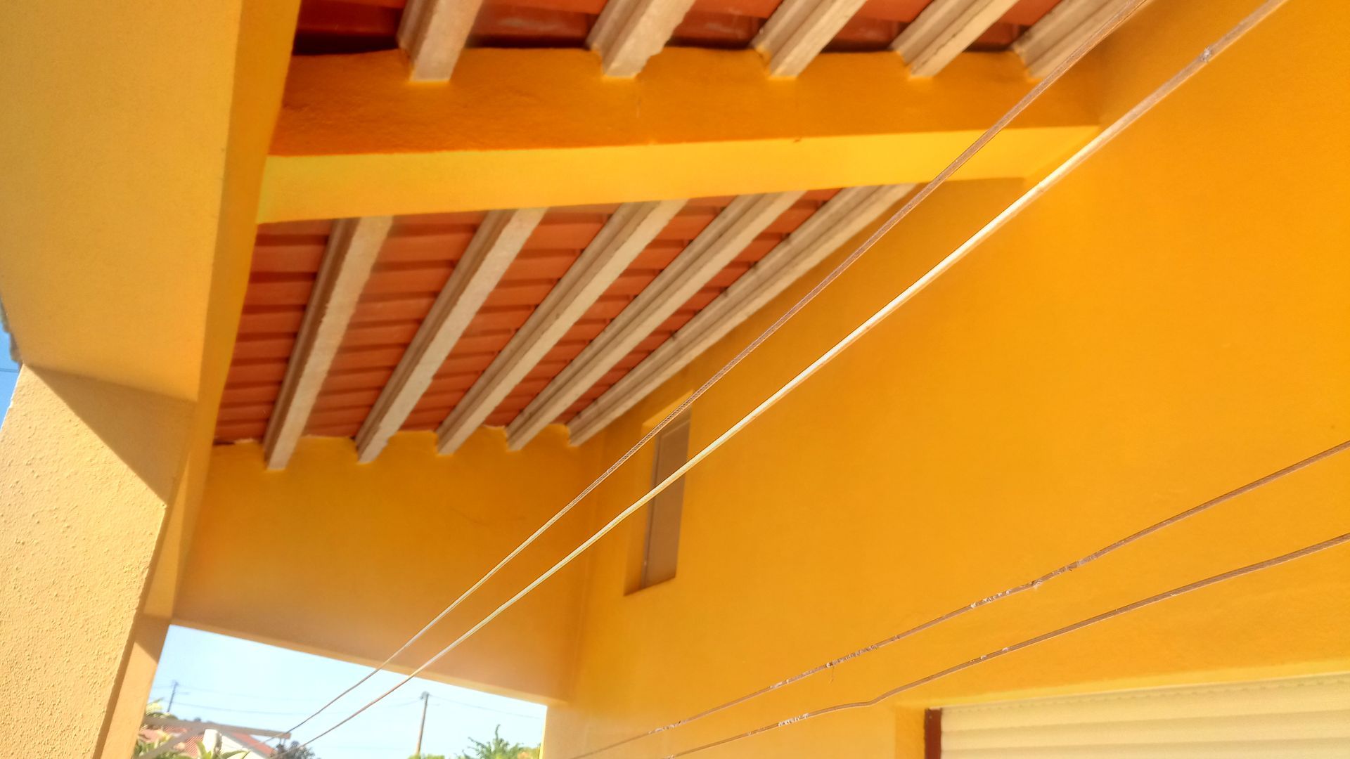 Varanda amarela com varais sob um telhado de telhas sustentado por vigas brancas.