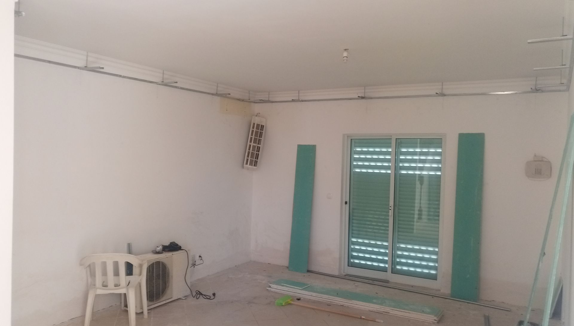 Quarto interior em construção, paredes brancas, porta de vidro deslizante, aparelho de ar condicionado, materiais de construção.